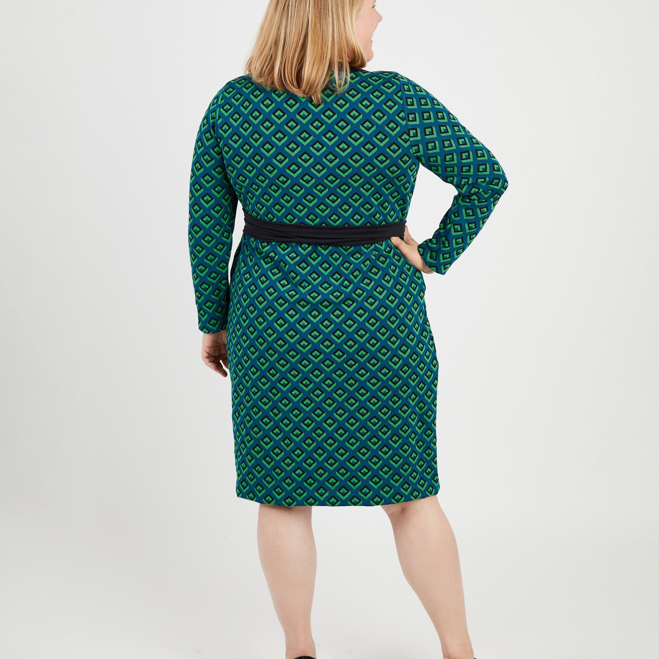 Woman wearing a green patterned dress on a white background. This dress is the Appleton Wrap Dress sewing pattern from Cashmerette.
