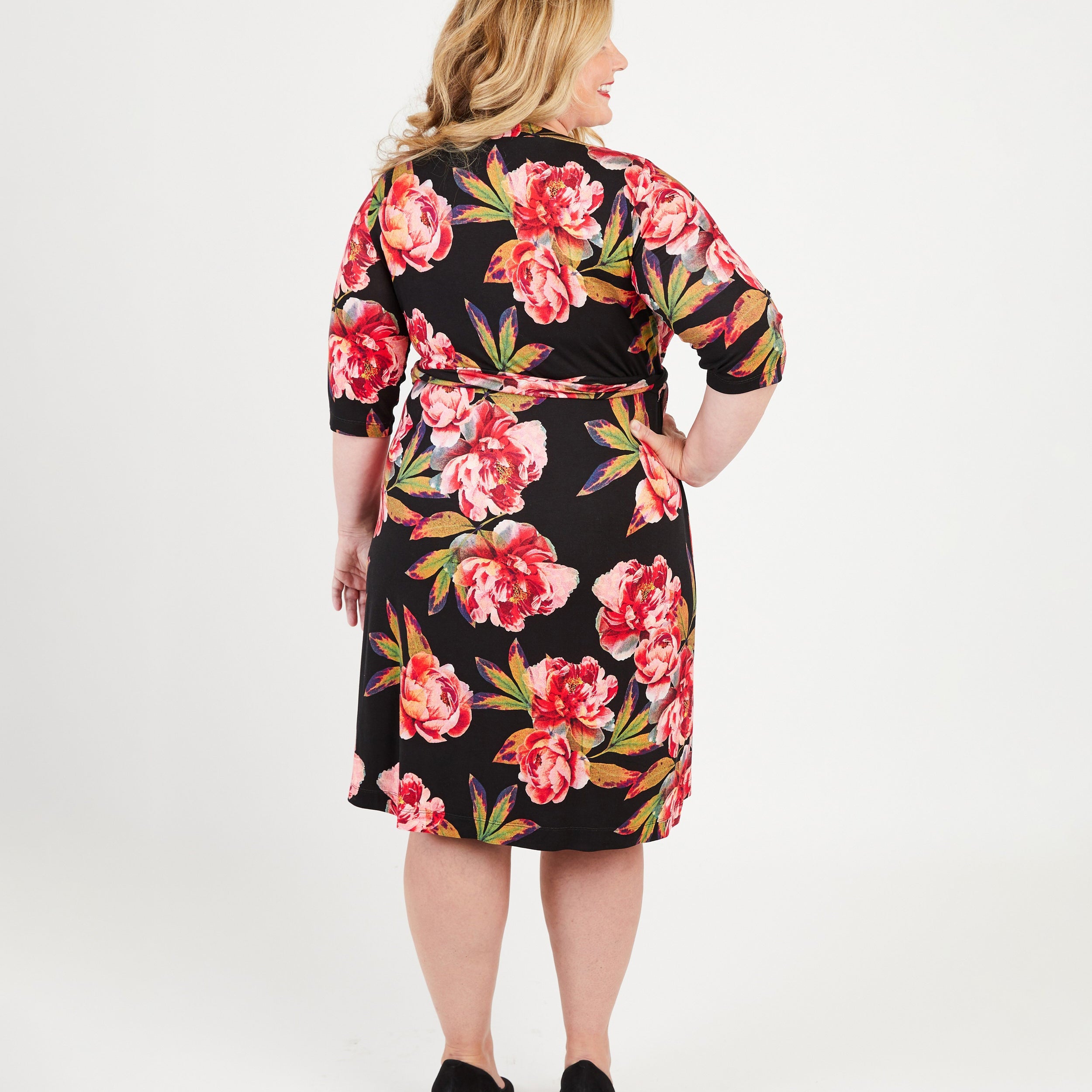 Woman wearing a black floral dress on a white background. This dress is the Appleton Wrap Dress sewing pattern from Cashmerette.
