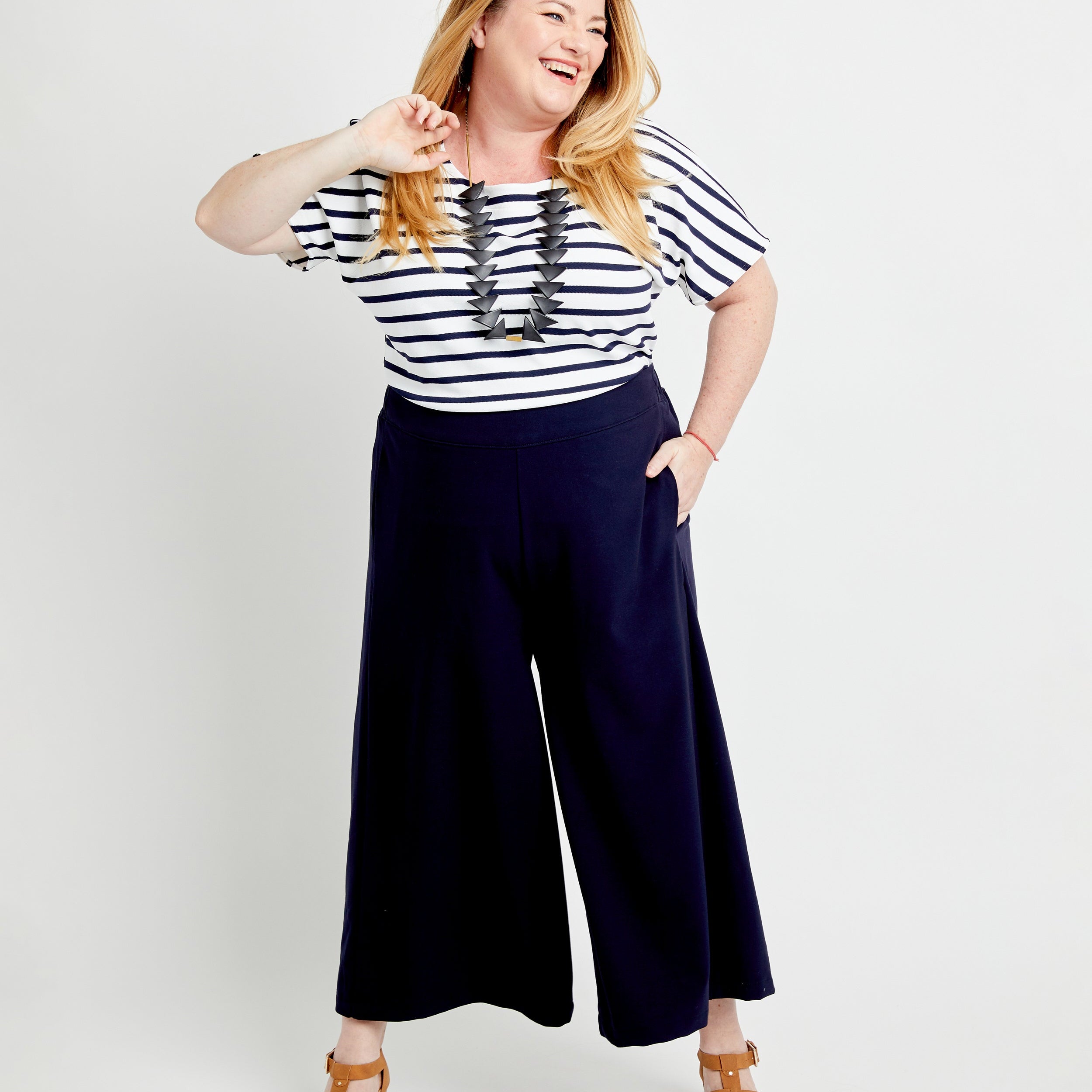 Woman wearing a striped shirt and navy wide-leg pants on a white background. These pants are the Calder Pants & Shorts sewing pattern from Cashmerette.