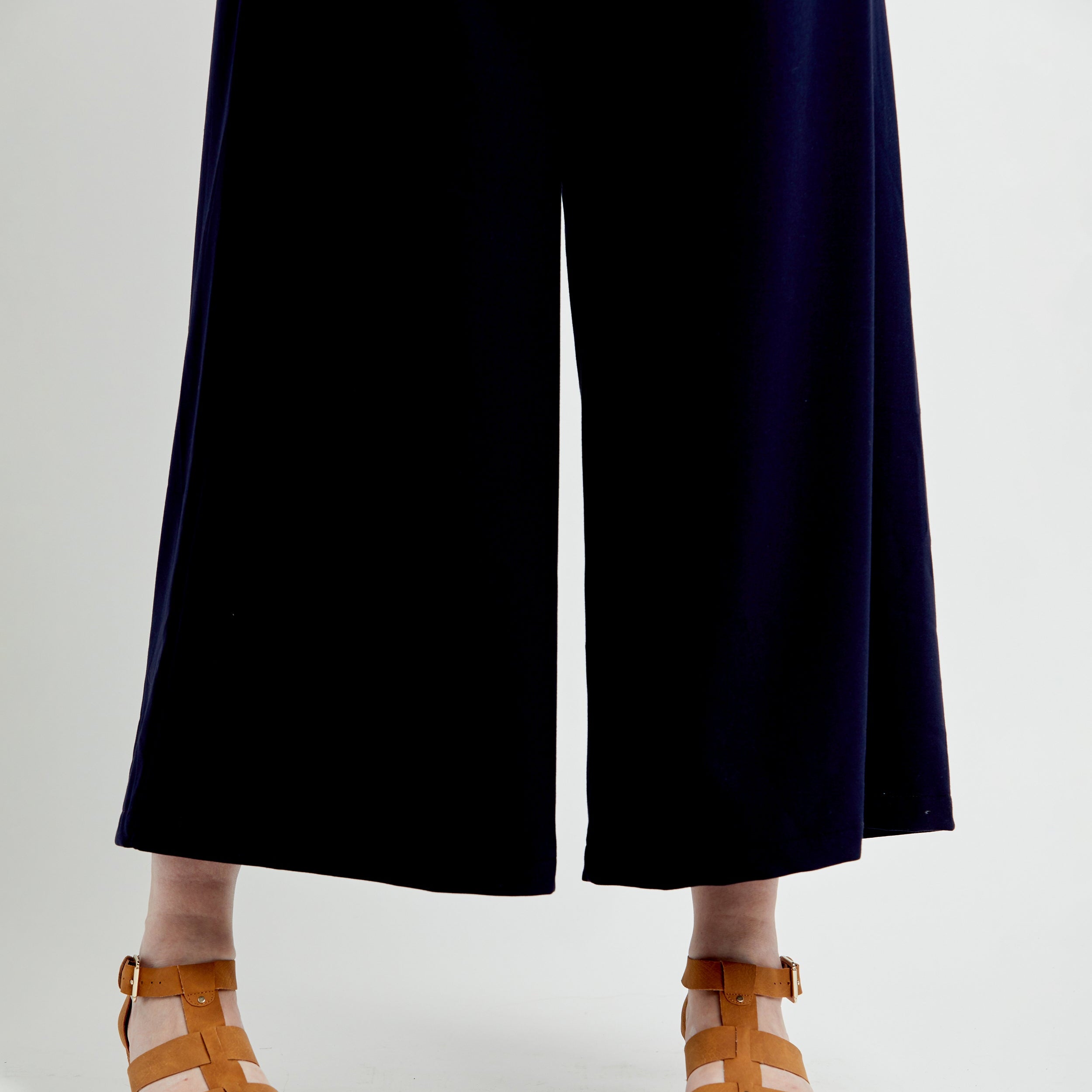 Person wearing navy blue pants and brown sandals on a white background. These pants are the Calder Pants & Shorts sewing pattern from Cashmerette.