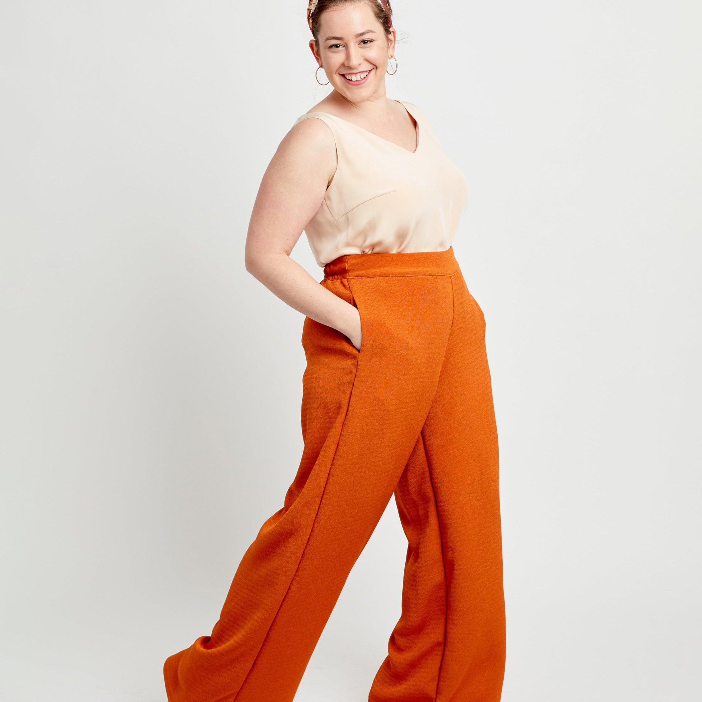 Woman wearing a beige top and orange wide-leg pants on a white background. These pants are the Calder Pants & Shorts sewing pattern from Cashmerette.