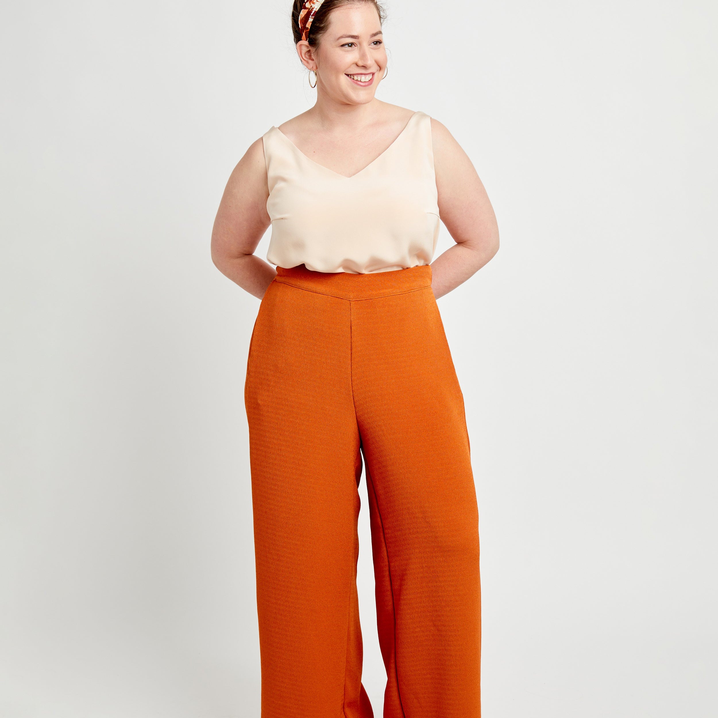 Woman wearing a beige top and orange pants on a white background. These pants are the Calder Pants & Shorts sewing pattern from Cashmerette.