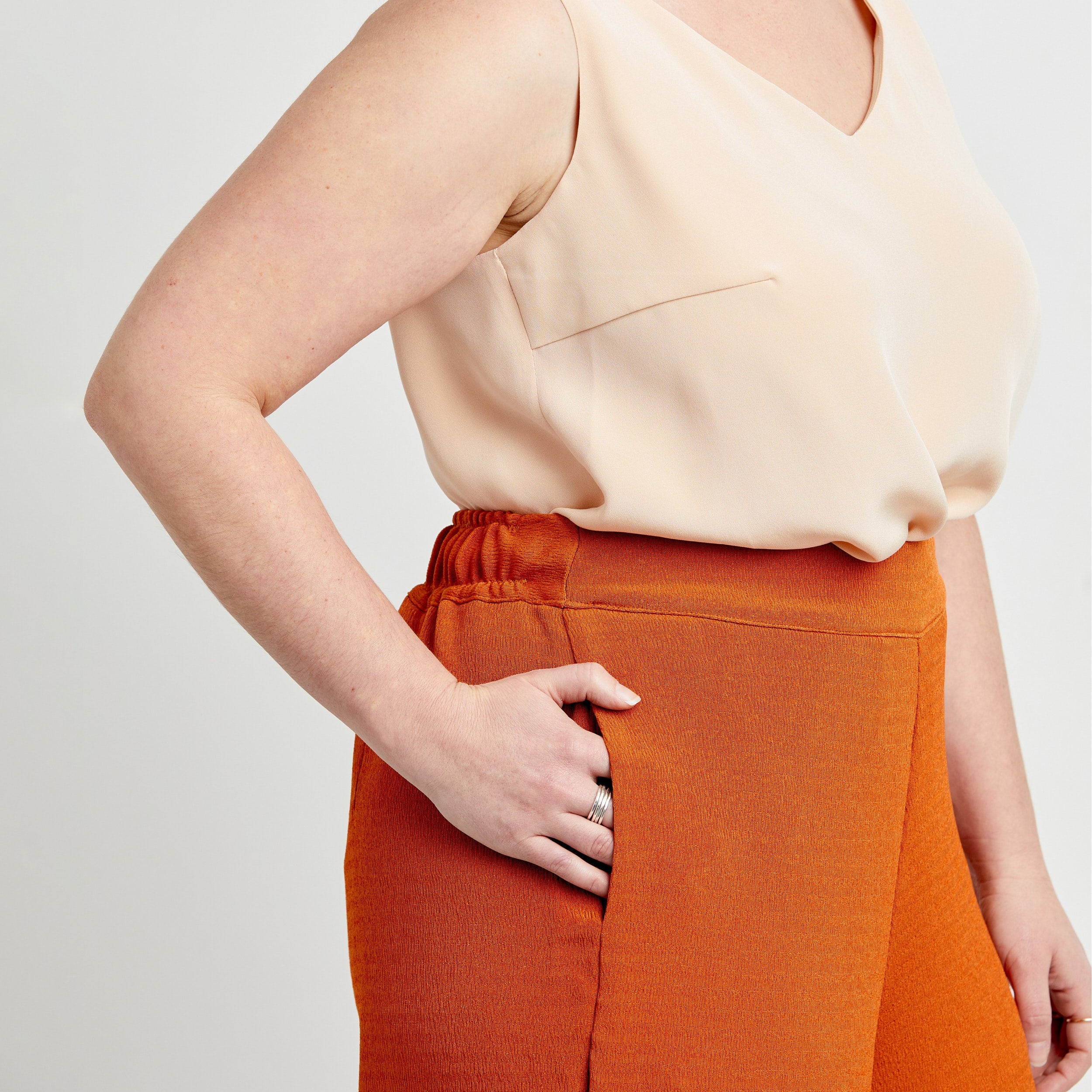 Person wearing a beige top and orange pants on a plain background. These pants are the Calder Pants & Shorts sewing pattern from Cashmerette.