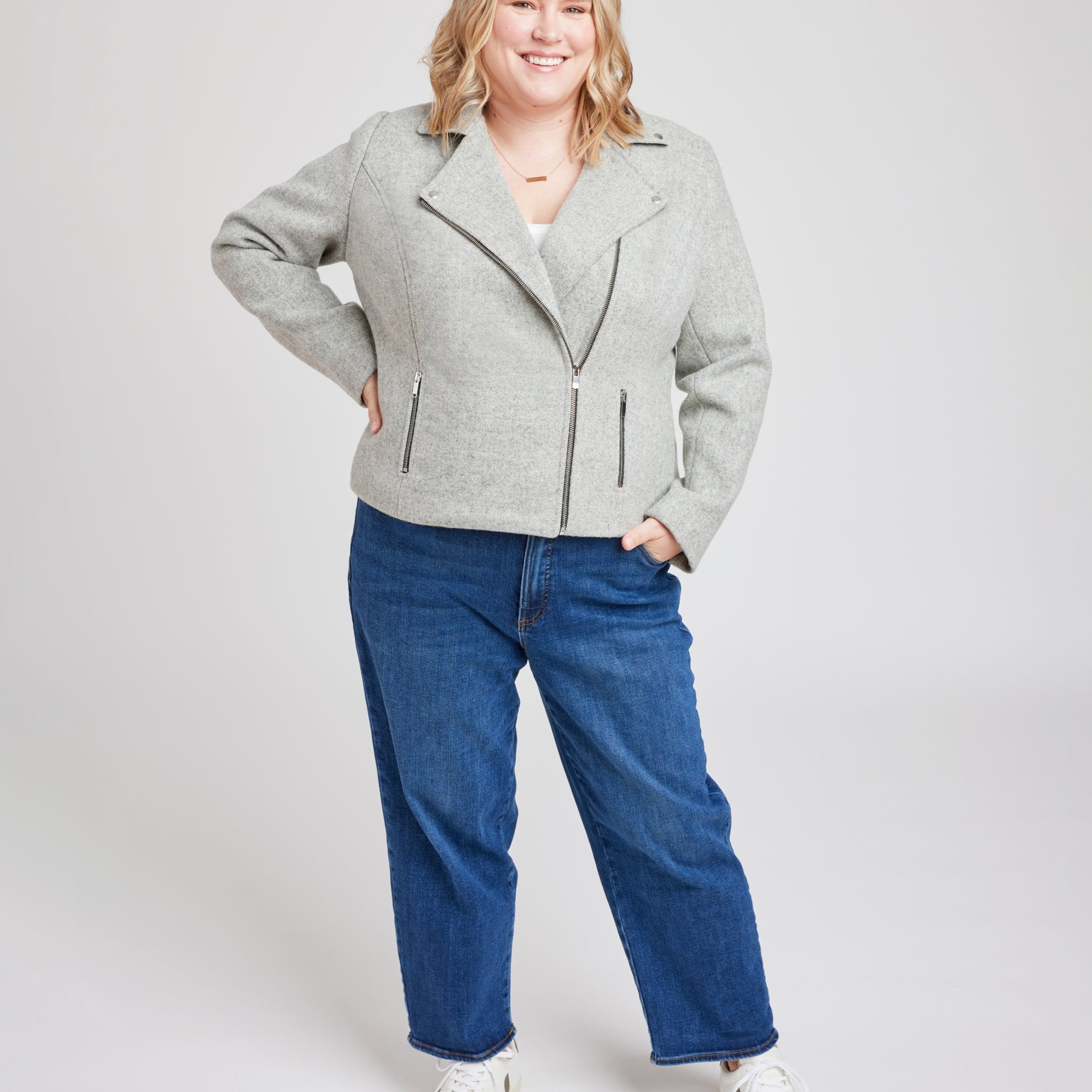 Woman wearing a gray jacket and blue jeans on a white background. This biker jacket is the Canton Moto Jacket sewing pattern from Cashmerette.