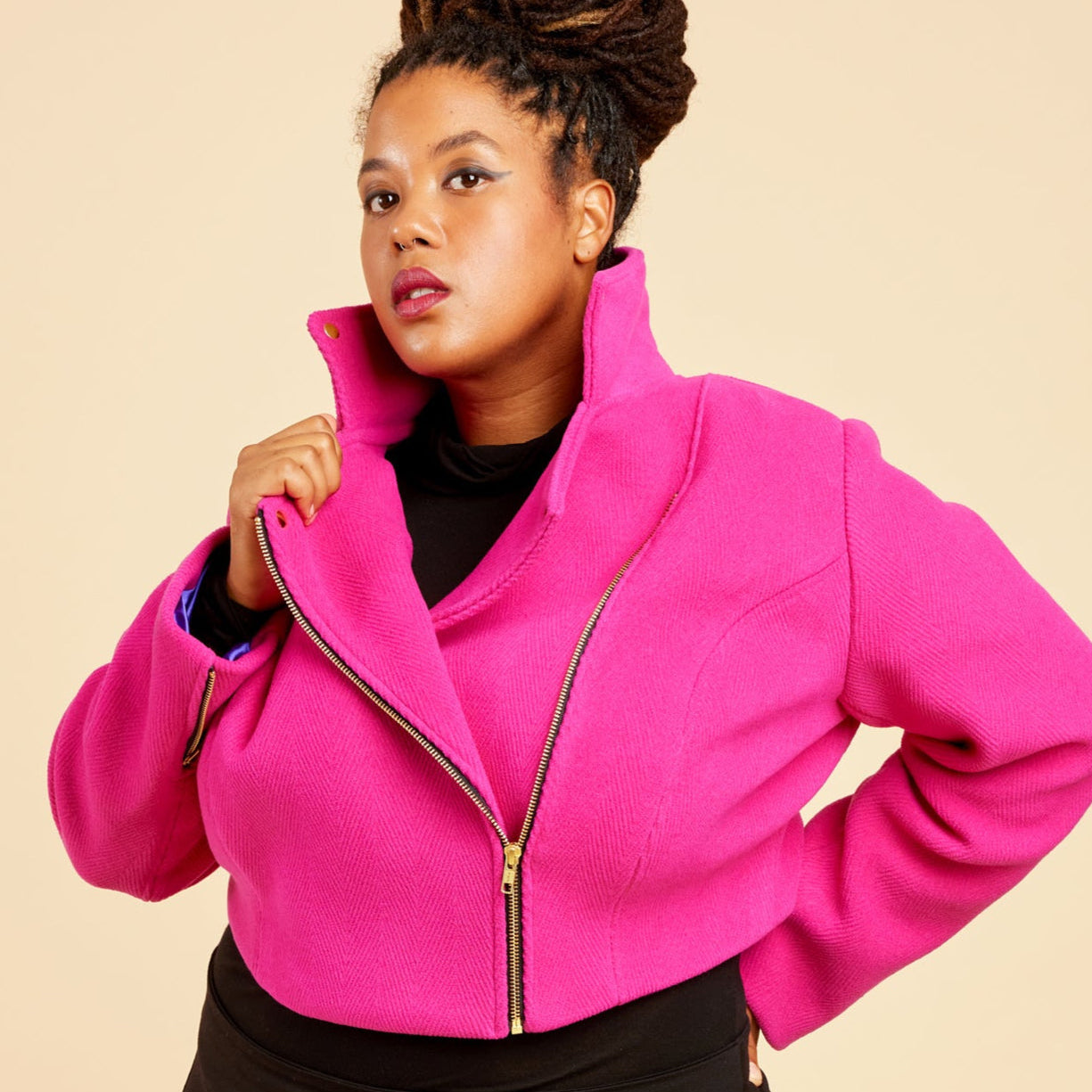 Person wearing a bright pink jacket and black pants on a beige background. This biker jacket is the Canton Moto Jacket sewing pattern from Cashmerette.