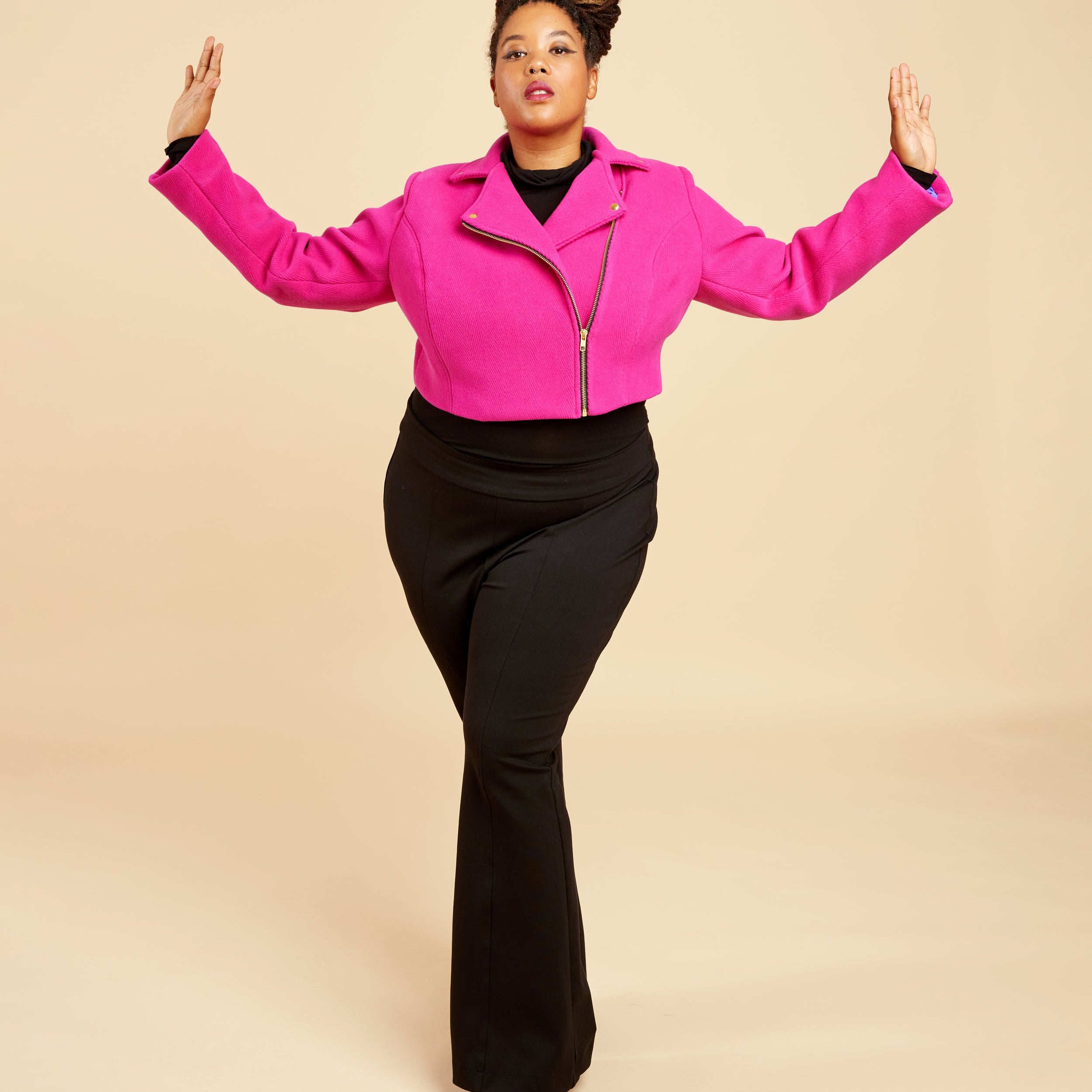 Person wearing a bright pink jacket and black pants on a beige background. This biker jacket is the Canton Moto Jacket sewing pattern from Cashmerette.