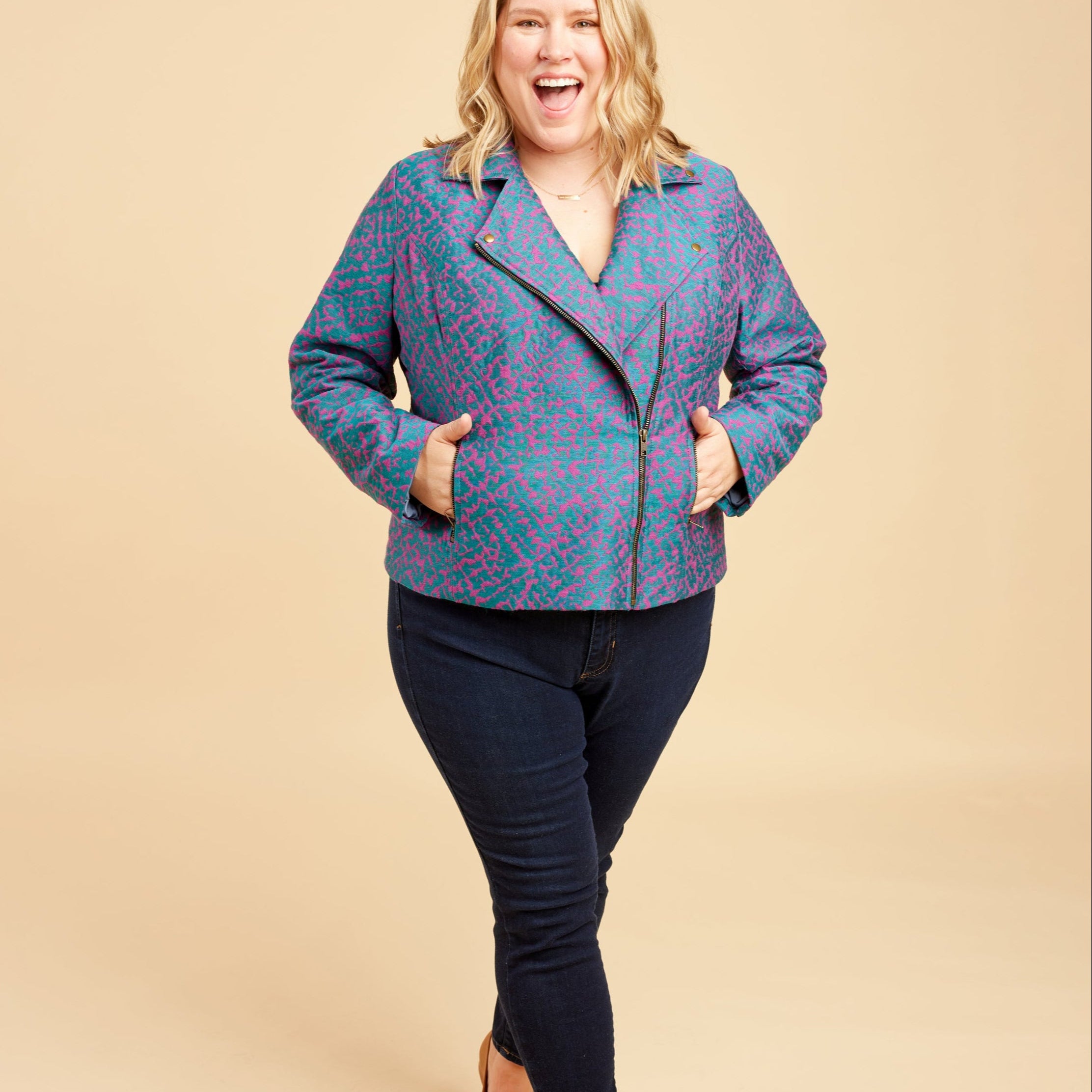 Woman wearing a blue patterned jacket and black pants on a beige background. This biker jacket is the Canton Moto Jacket sewing pattern from Cashmerette.