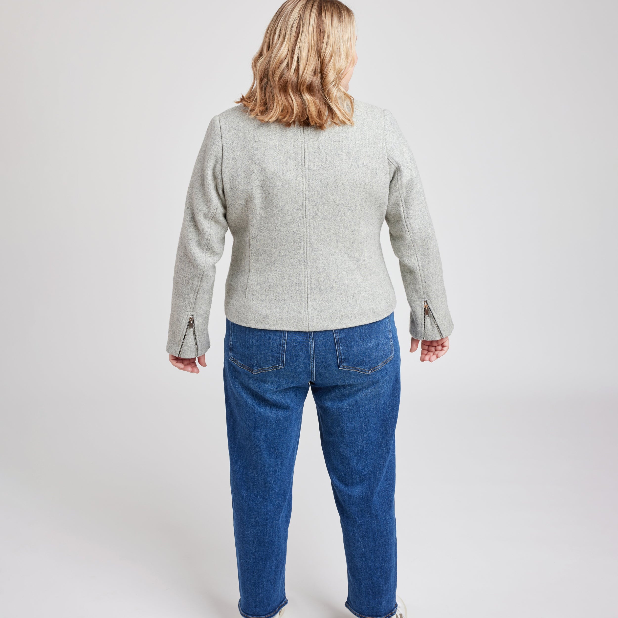 Person wearing a gray jacket and blue jeans on a white background. This biker jacket is the Canton Moto Jacket sewing pattern from Cashmerette.
