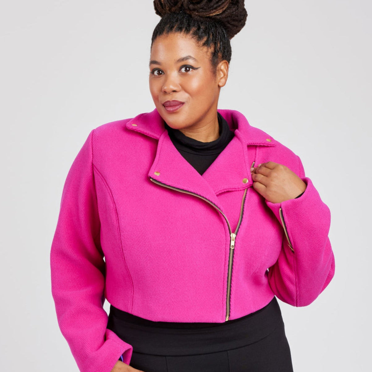 Woman wearing a bright pink jacket with a plain background. This biker jacket is the Canton Moto Jacket sewing pattern from Cashmerette.