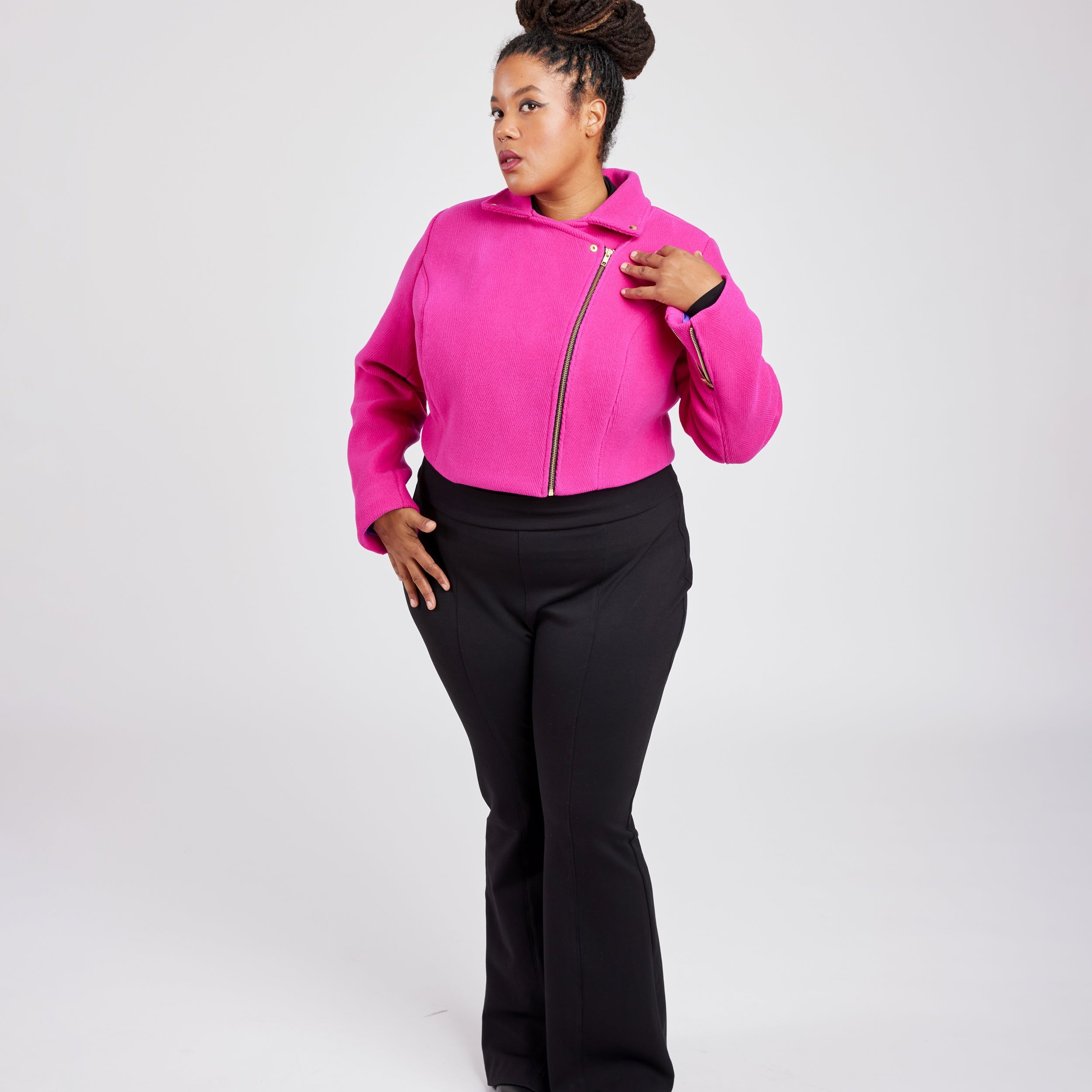 Person wearing a bright pink hoodie with a zipper and black pants on a white background. This biker jacket is the Canton Moto Jacket sewing pattern from Cashmerette.