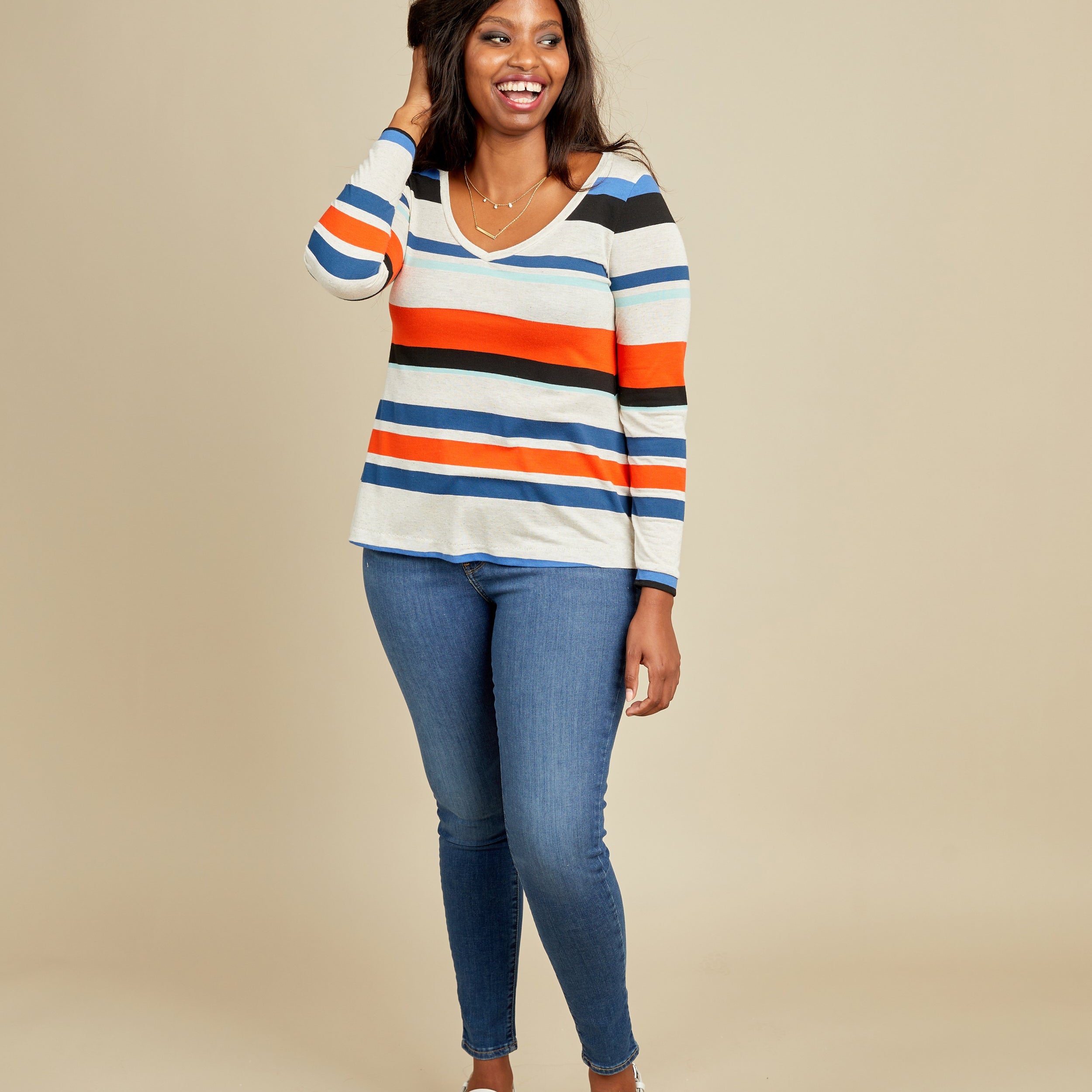 Woman wearing a striped sweater and blue jeans on a beige background. This t-shirt is the Concord T-Shirt sewing pattern from Cashmerette.