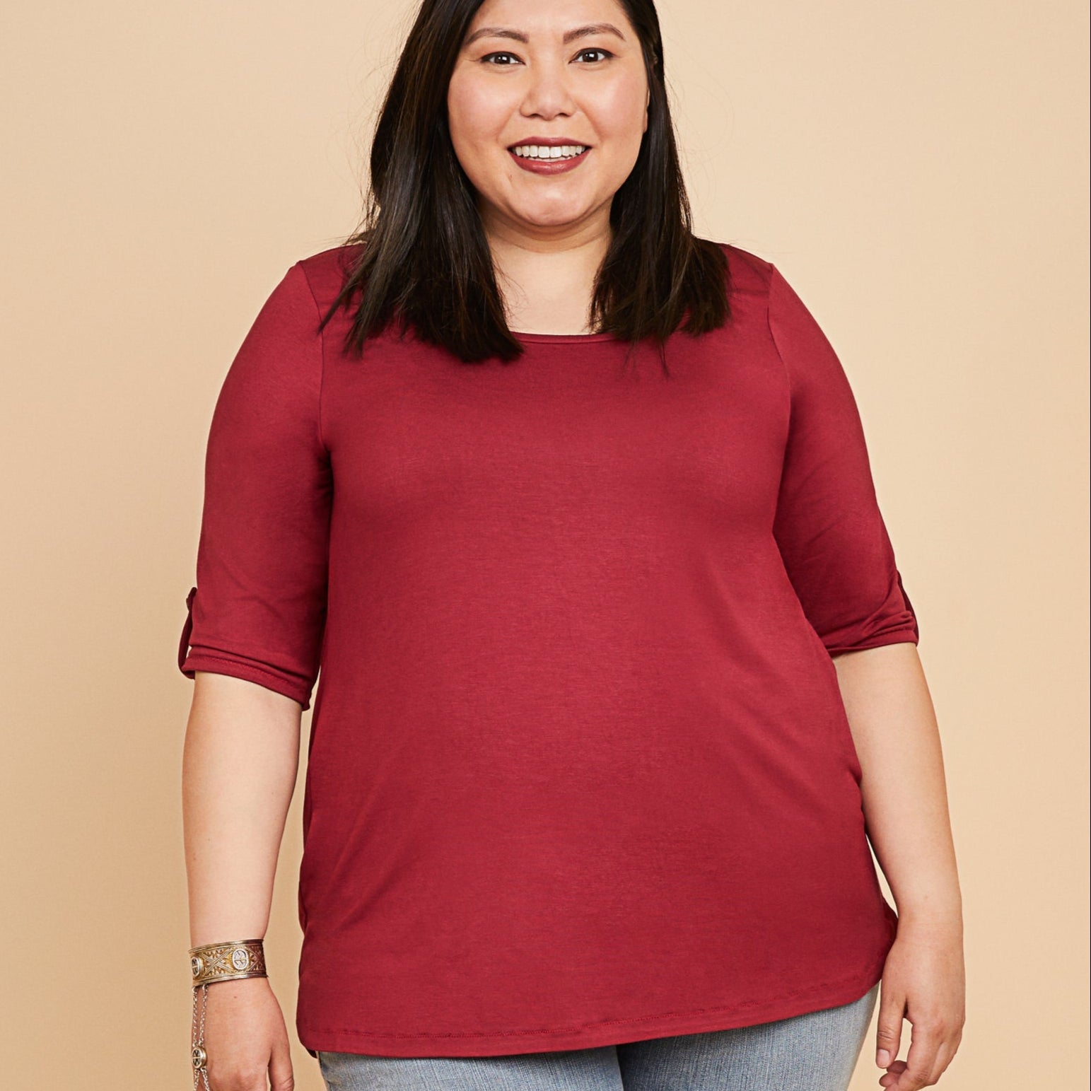 Woman wearing a red top and blue jeans on a beige background. This t-shirt is the Concord T-Shirt sewing pattern from Cashmerette.