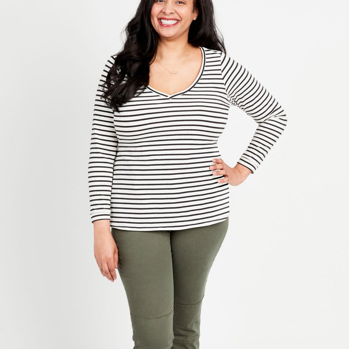 A woman standing, wearing a striped long-sleeved t-shirt and green pants. This t-shirt is the Concord T-Shirt sewing pattern from Cashmerette.