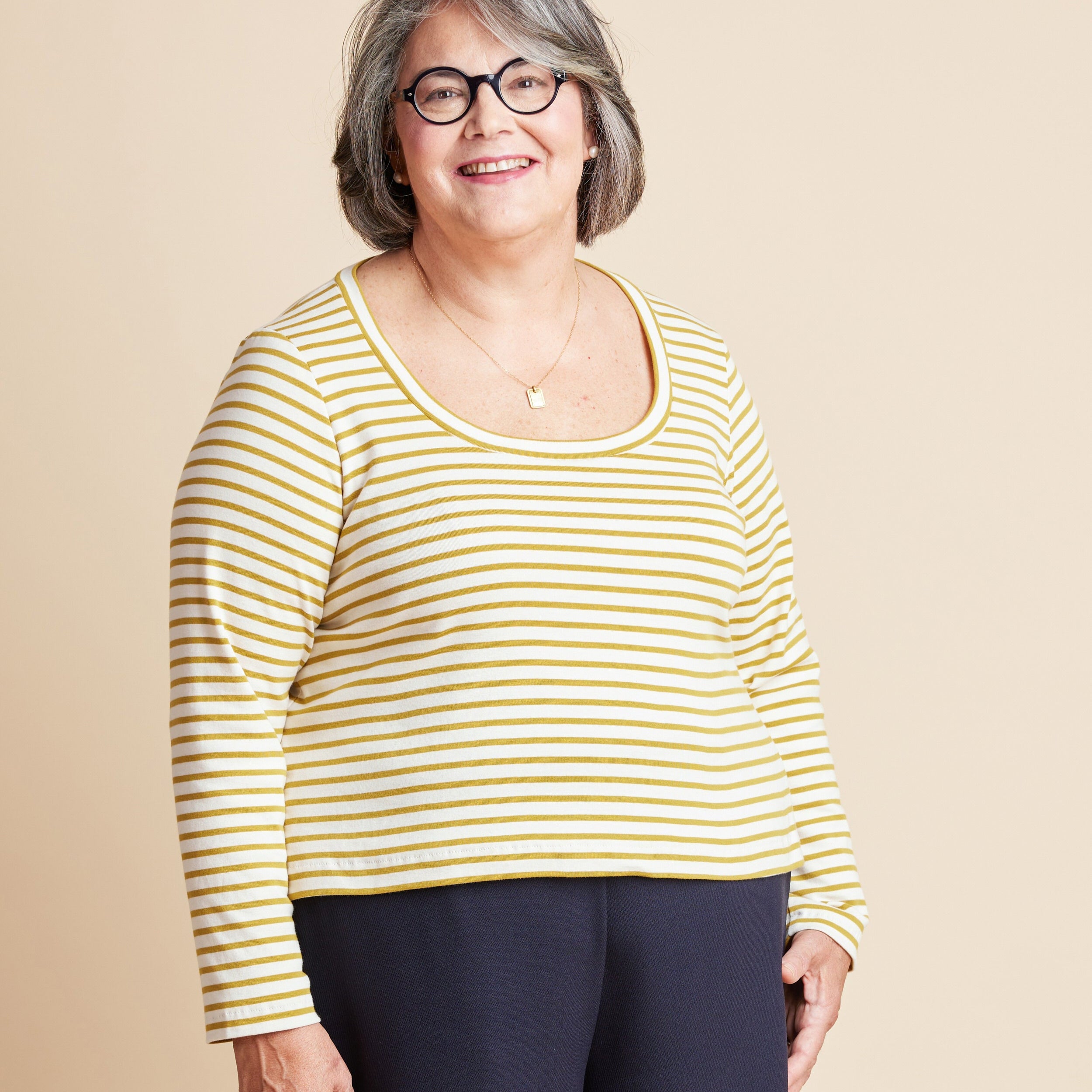 Woman wearing a yellow and white striped shirt against a beige background. This is the Grafton Dress, Top & Skirt sewing pattern from Cashmerette.