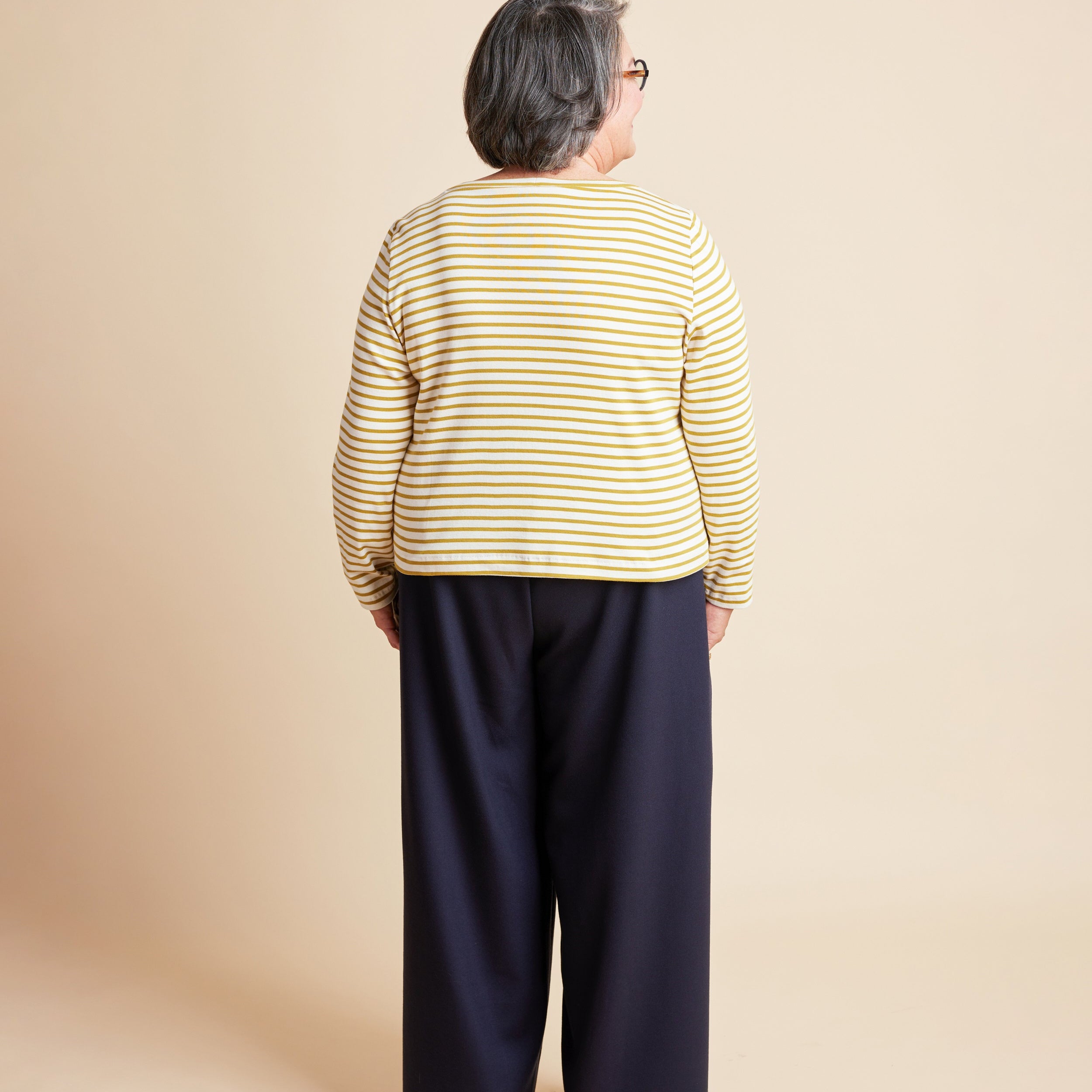 Person wearing a yellow striped shirt and navy pants on a beige background. This is the Grafton Dress, Top & Skirt sewing pattern from Cashmerette.