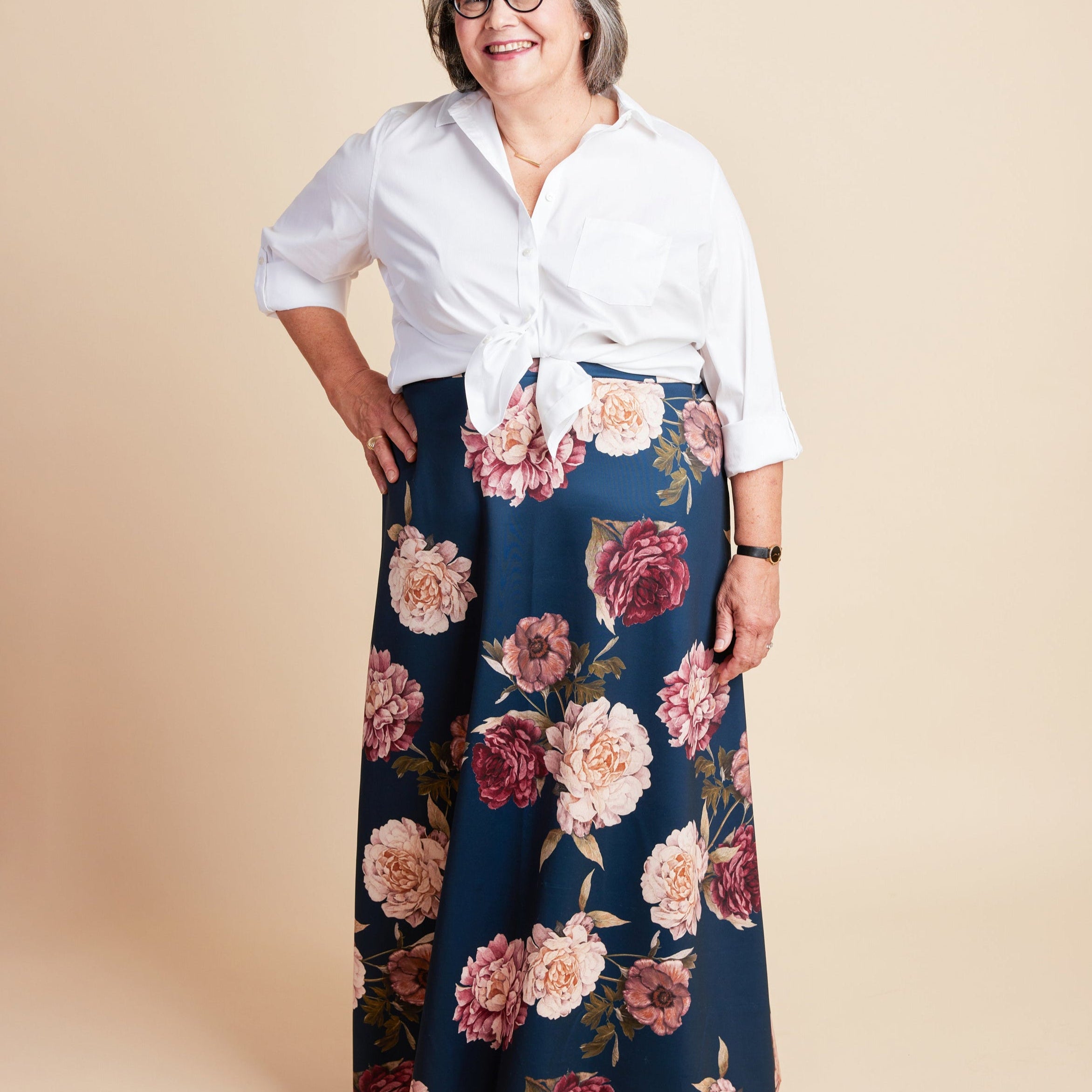 Woman wearing a white blouse and floral skirt on a beige background. This is the Grafton Dress, Top & Skirt sewing pattern from Cashmerette.