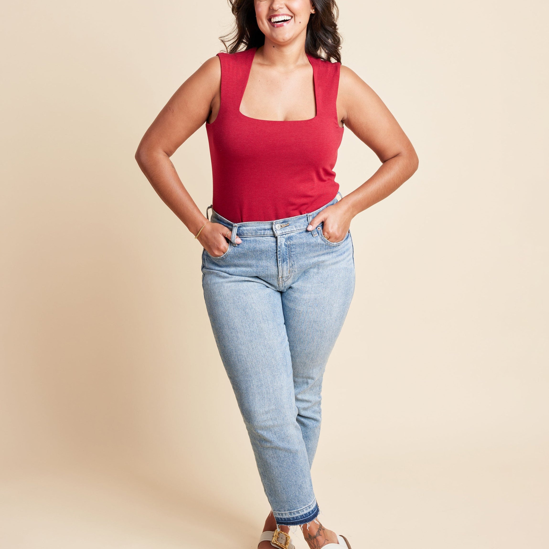 Woman wearing a red tank top and blue jeans against a beige background. This is the Grafton Dress, Top & Skirt sewing pattern from Cashmrette.
