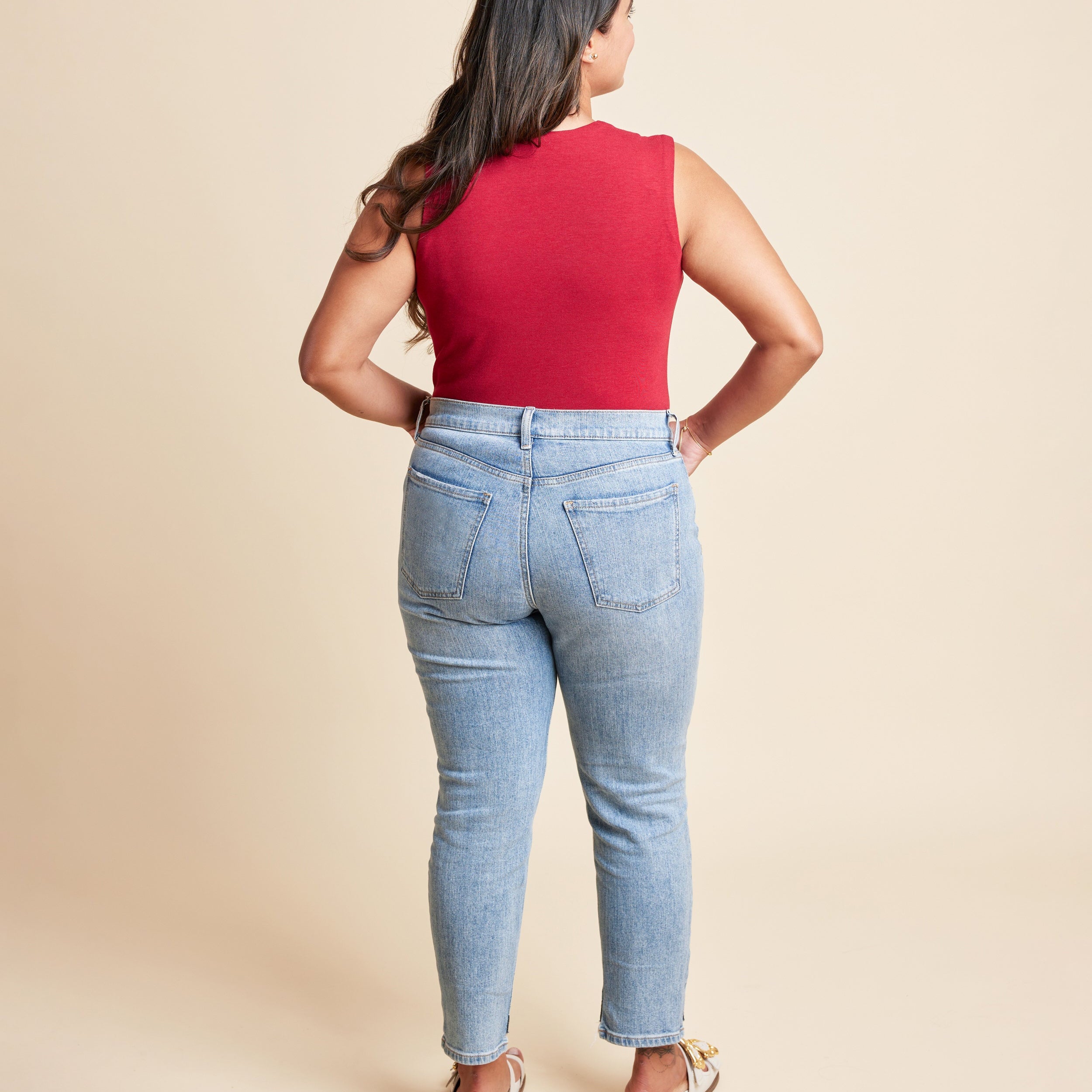 Woman wearing a red sleeveless top and light blue jeans on a beige background. This is the Grafton Dress, Top & Skirt sewing pattern from Cashmrette.