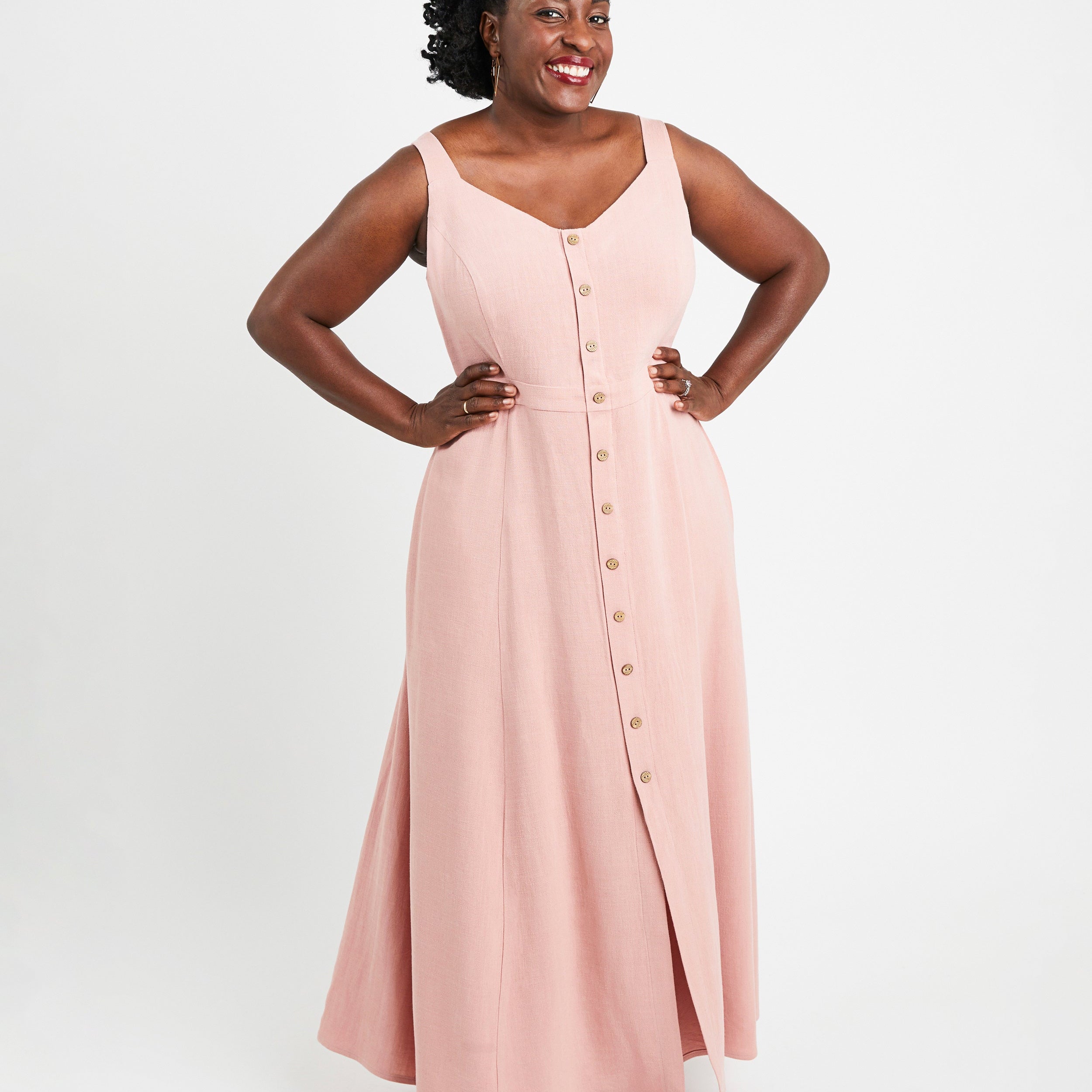 Woman wearing a pink sleeveless dress with buttons on a white background. This is the Holyoke Maxi Dress & Skirt sewing pattern from Cashmerette.