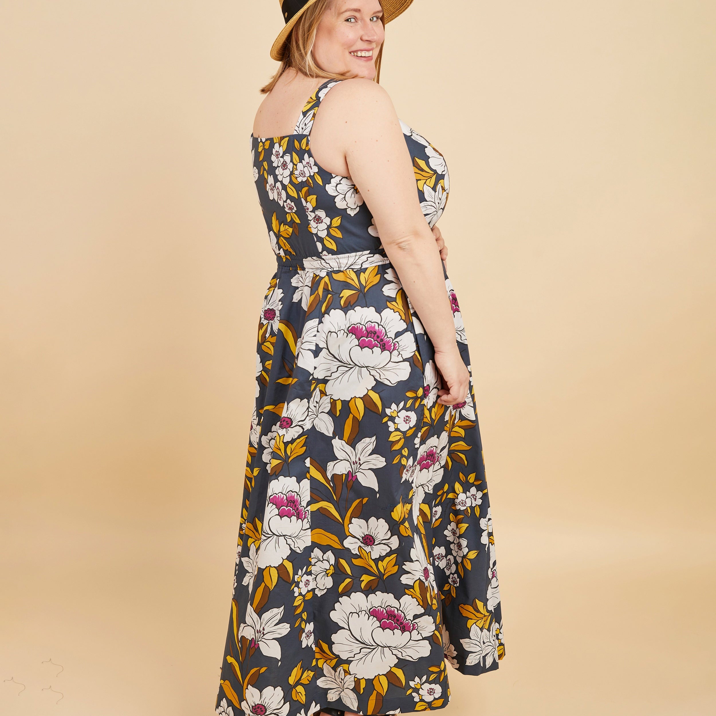 Woman wearing a floral dress and straw hat on a beige background. This is the Holyoke Maxi Dress & Skirt sewing pattern from Cashmerette.