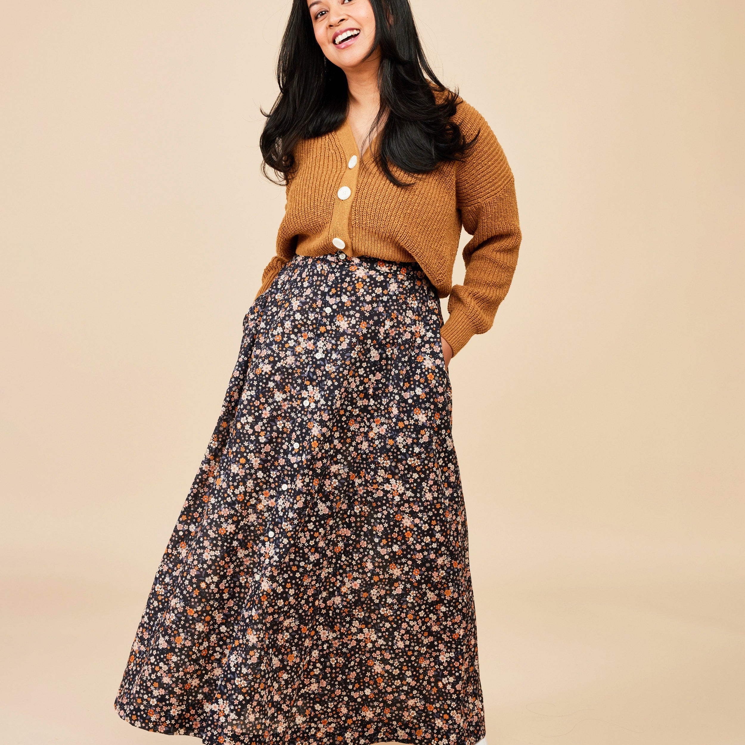 Woman wearing a mustard yellow cardigan and floral skirt on a beige background. This is the Holyoke Maxi Dress & Skirt sewing pattern from Cashmerette.