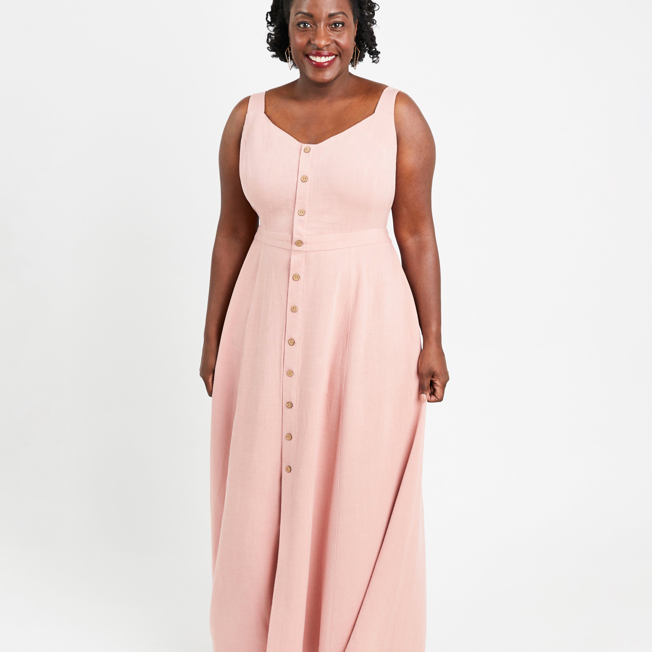 Woman wearing a pink sleeveless dress with buttons on a white background. This is the Holyoke Maxi Dress & Skirt sewing pattern from Cashmerette.