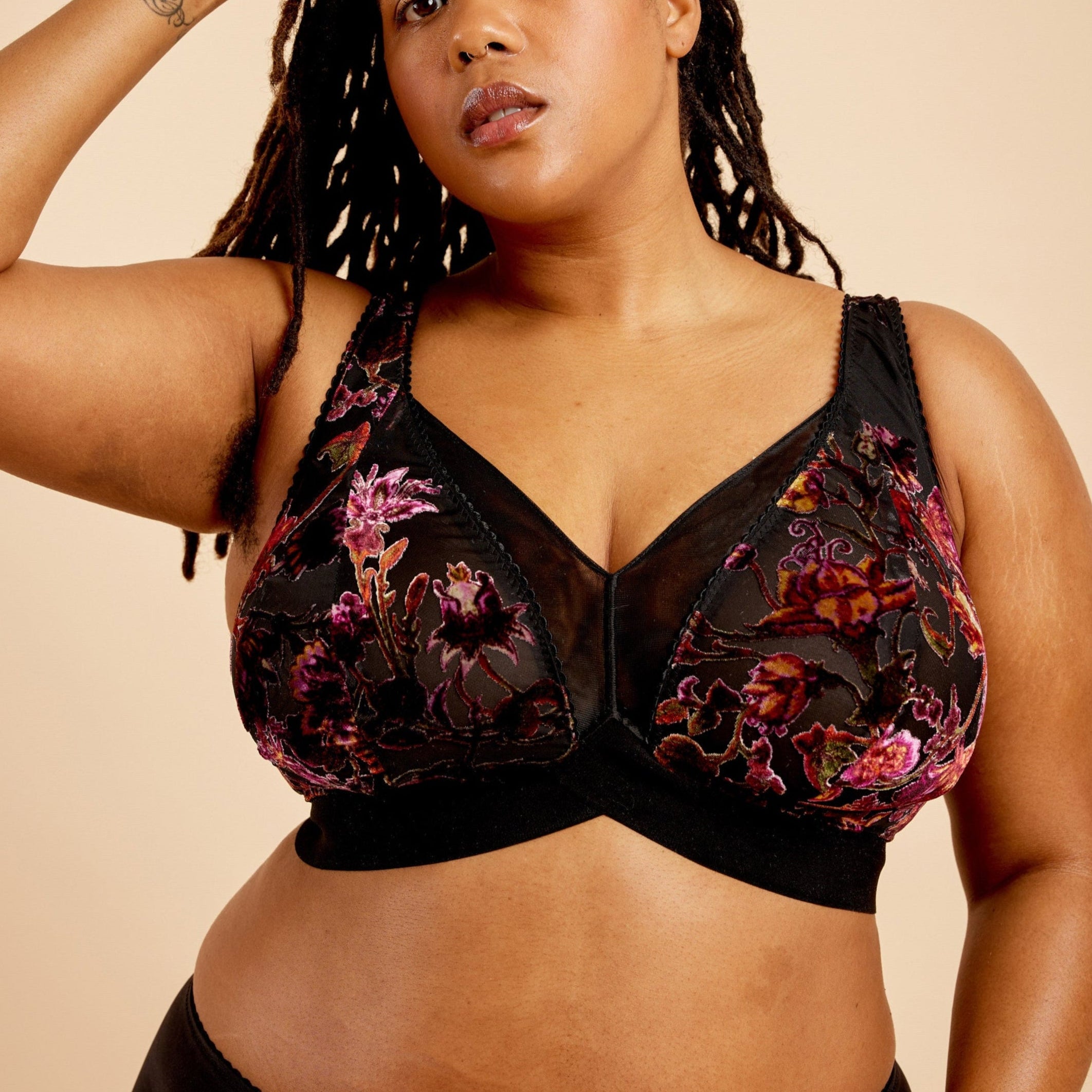 Woman wearing a black floral lingerie set against a beige background. This bralette is the Loftus Bralette sewing pattern from Cashmerette.