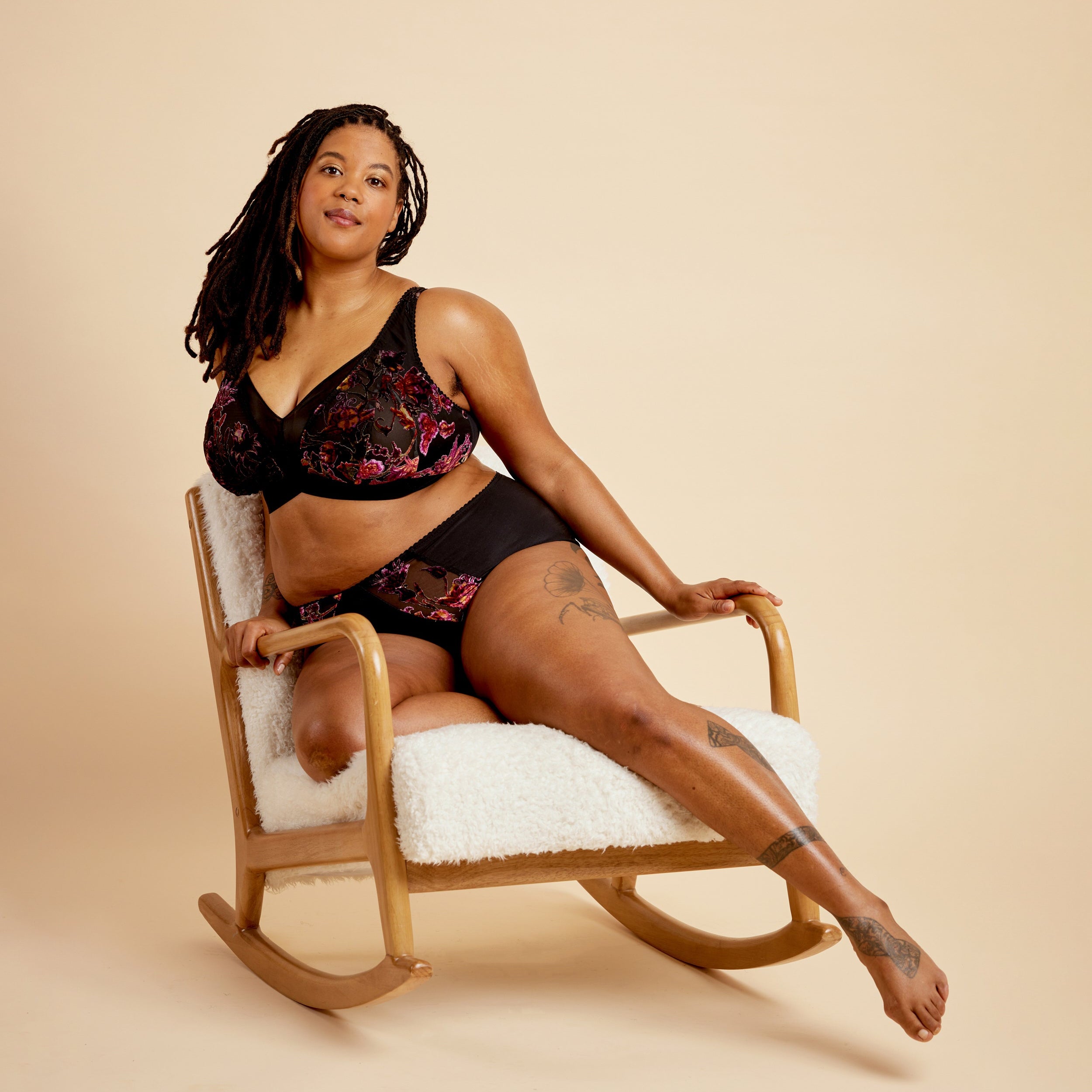 Woman in black lingerie sitting on a rocking chair against a beige background. This bralette is the Loftus Bralette sewing pattern from Cashmerette.