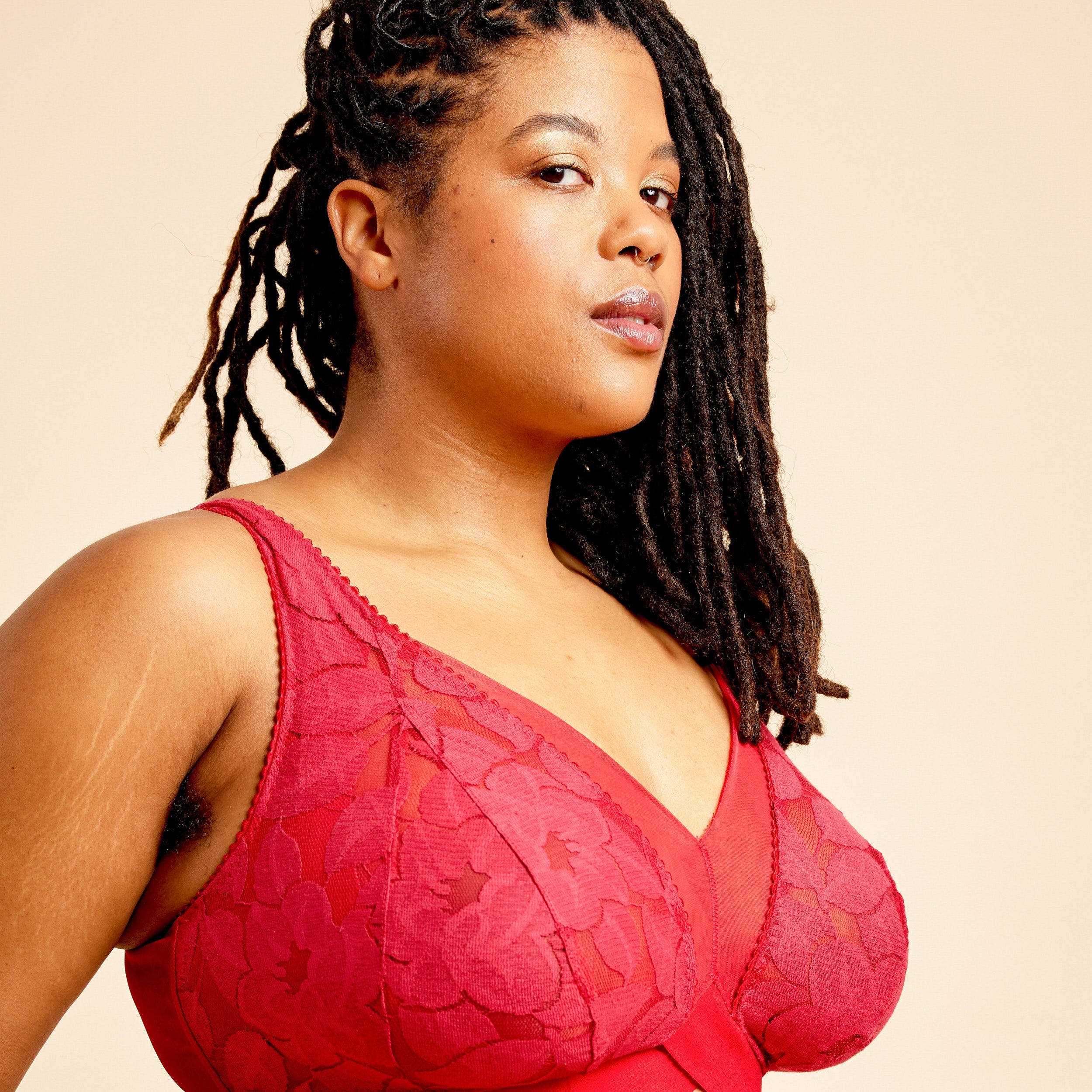 Woman wearing a red lace bralette against a beige background. This bralette is the Loftus Bralette sewing pattern from Cashmerette.