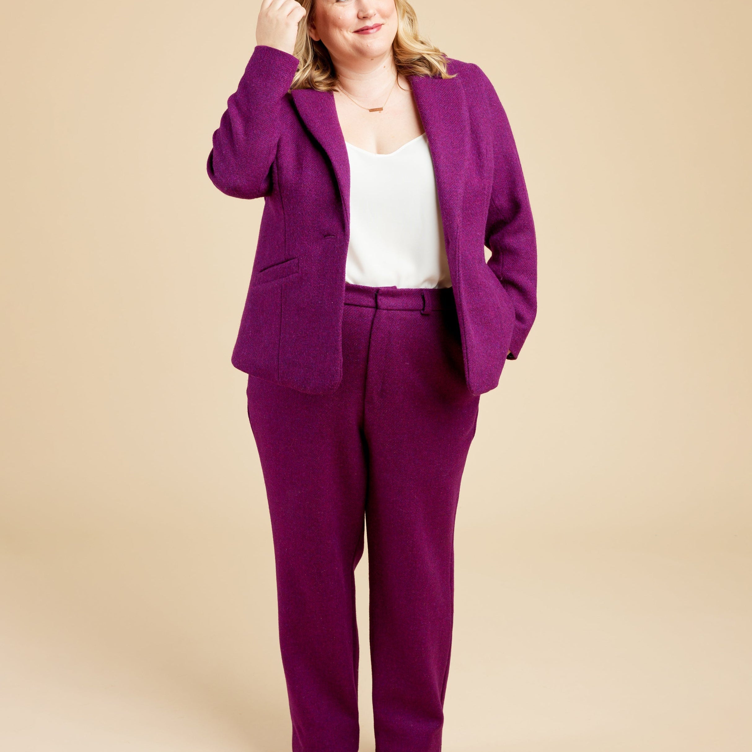 Woman wearing a purple suit with a beige background. These pants are the Meriam Trousers sewing pattern from Cashmerette.