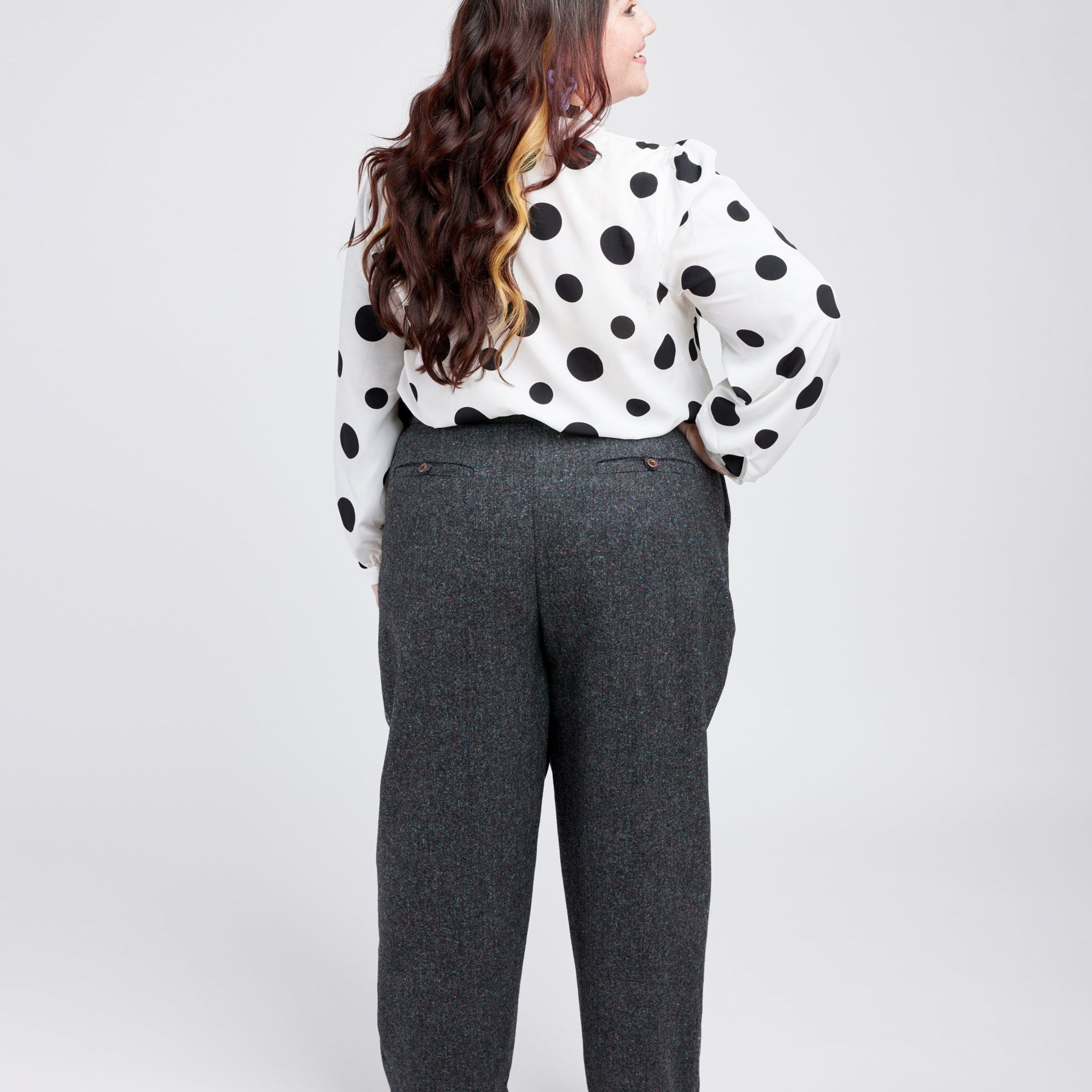 Person wearing a polka dot blouse and gray pants on a white background. These pants are the Meriam Trousers sewing pattern from Cashmerette.