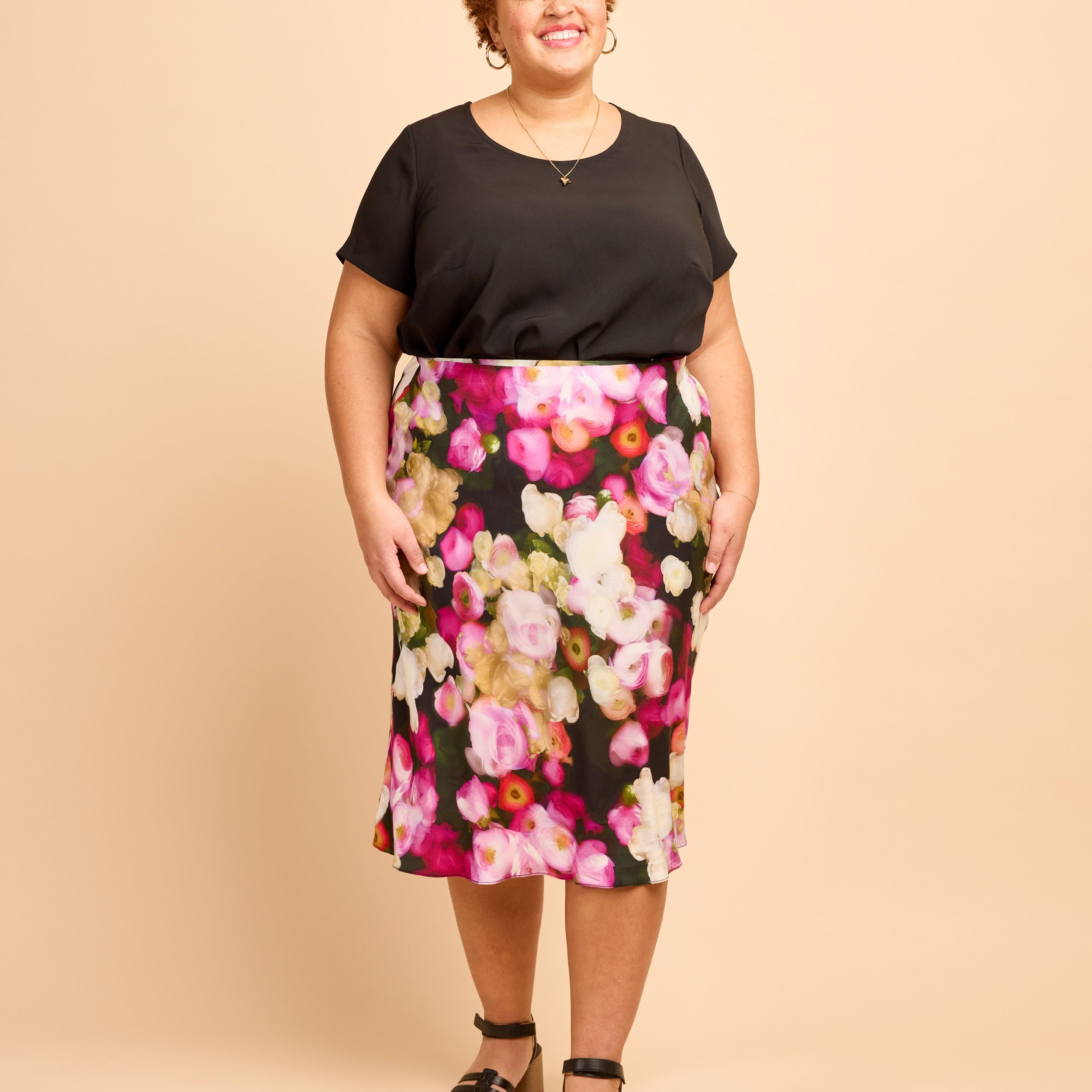 Woman wearing a black top and floral skirt on a beige background. This is the Montrose Top sewing pattern from Cashmerette.