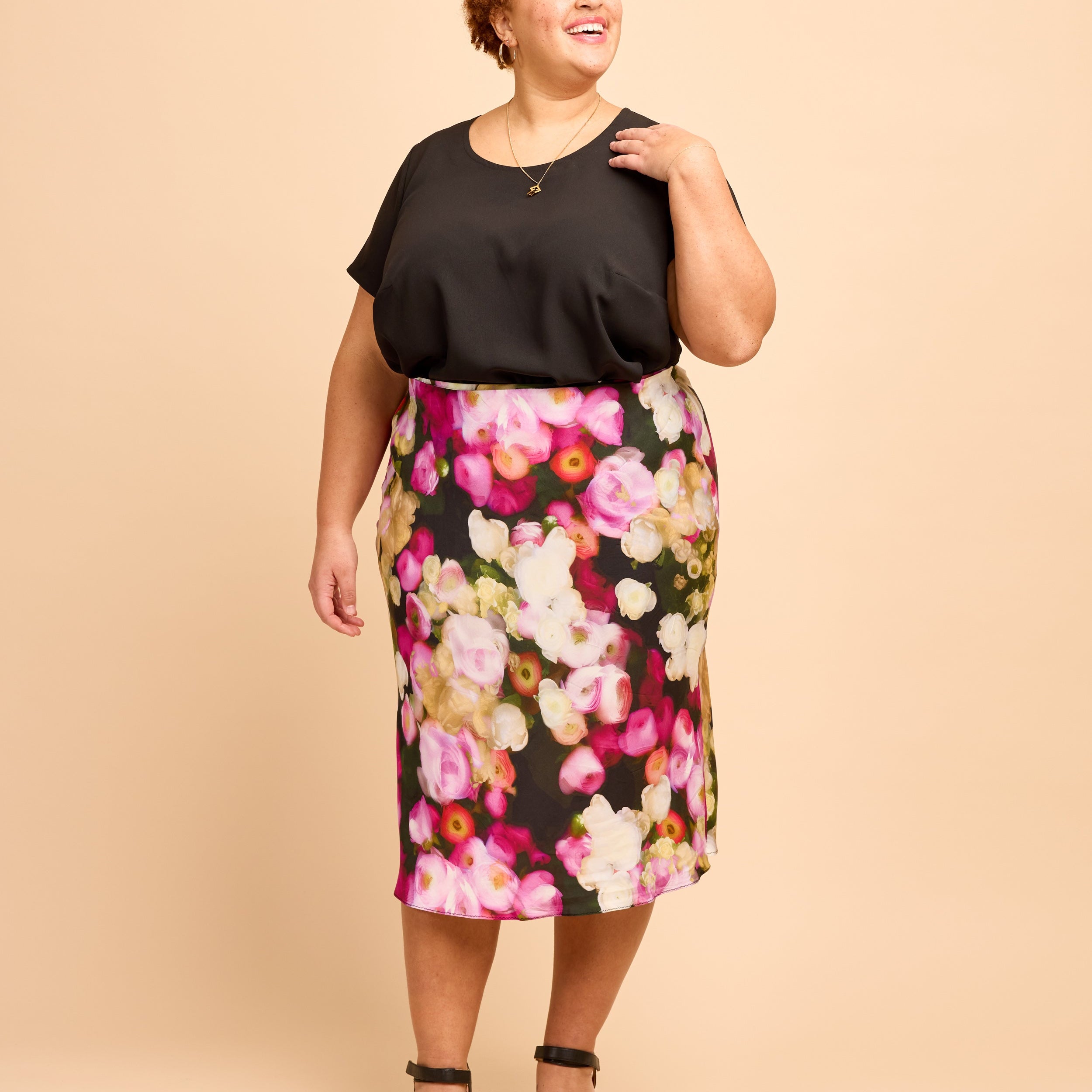 Woman wearing a black top and floral skirt on a beige background. This is the Montrose Top sewing pattern from Cashmerette.