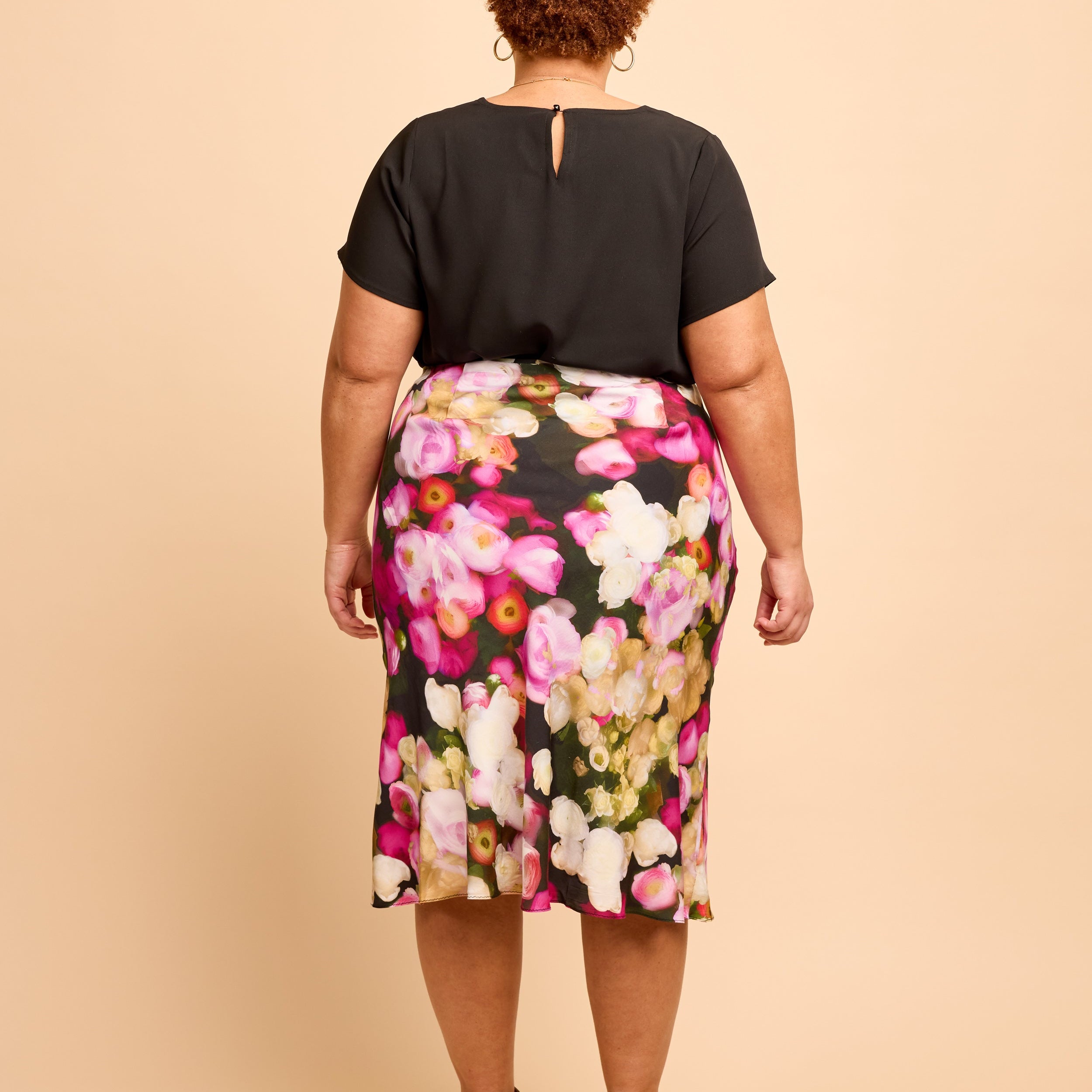 Person wearing a black top and floral skirt on a beige background. This is the Montrose Top sewing pattern from Cashmerette.