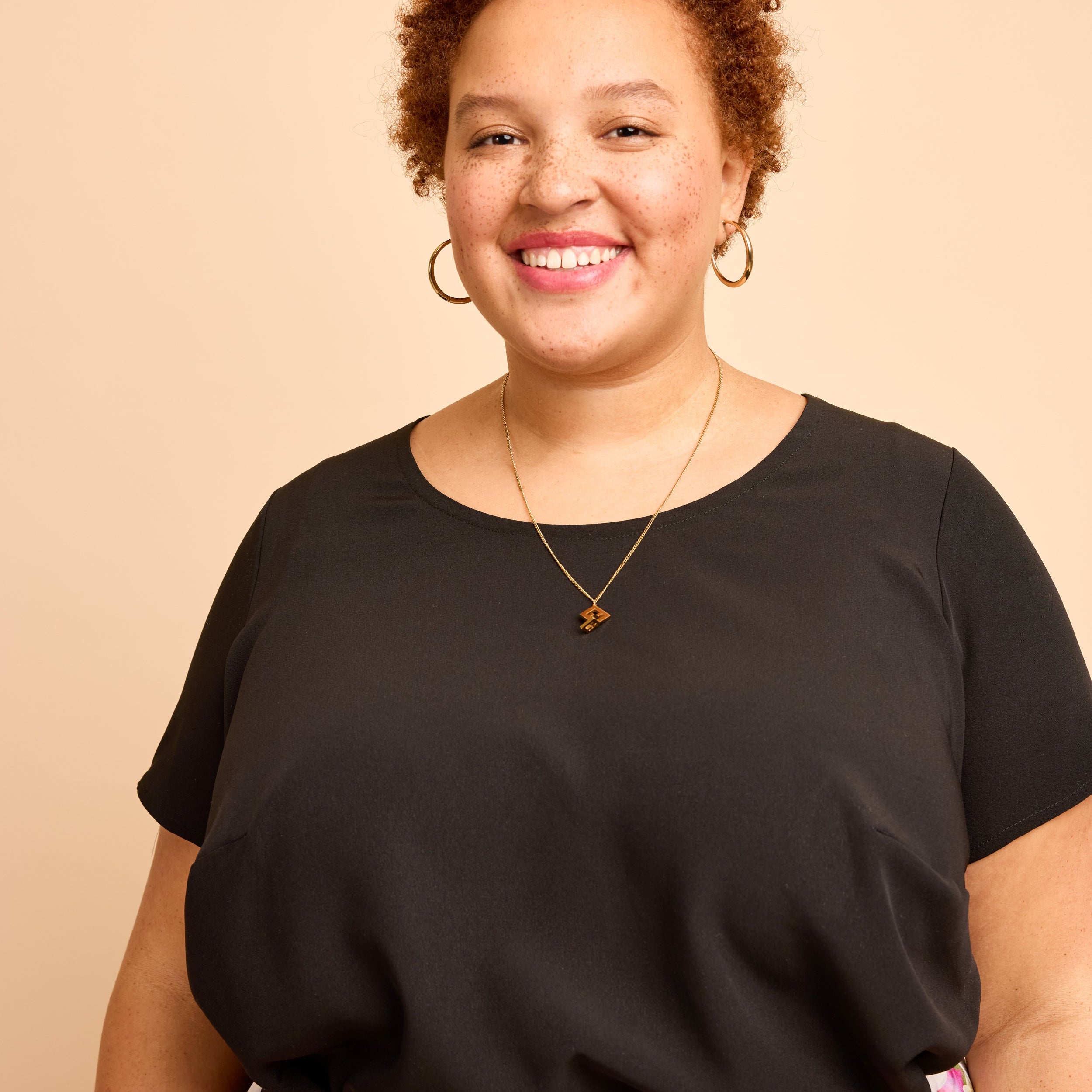 Woman wearing a black top with floral pants against a beige background. This is the Montrose Top sewing pattern from Cashmerette.
