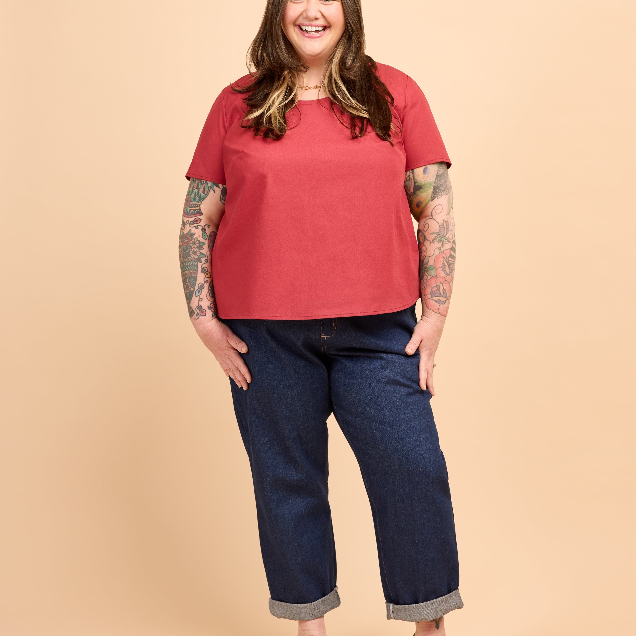 Person wearing a red shirt and blue jeans on a beige background. This is the Montrose Top sewing pattern from Cashmerette.