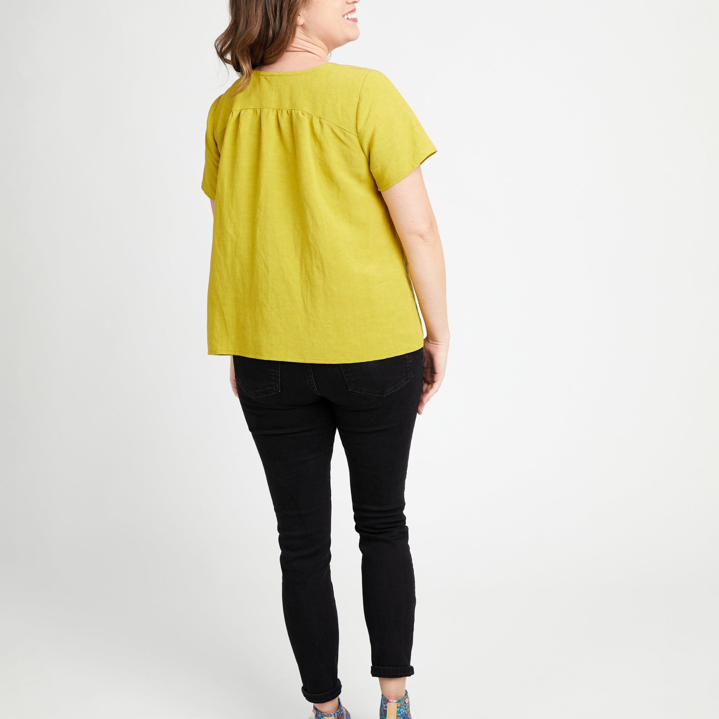 Woman wearing a yellow top and black pants on a white background. This top is the Montrose Top sewing pattern from Cashmerette.