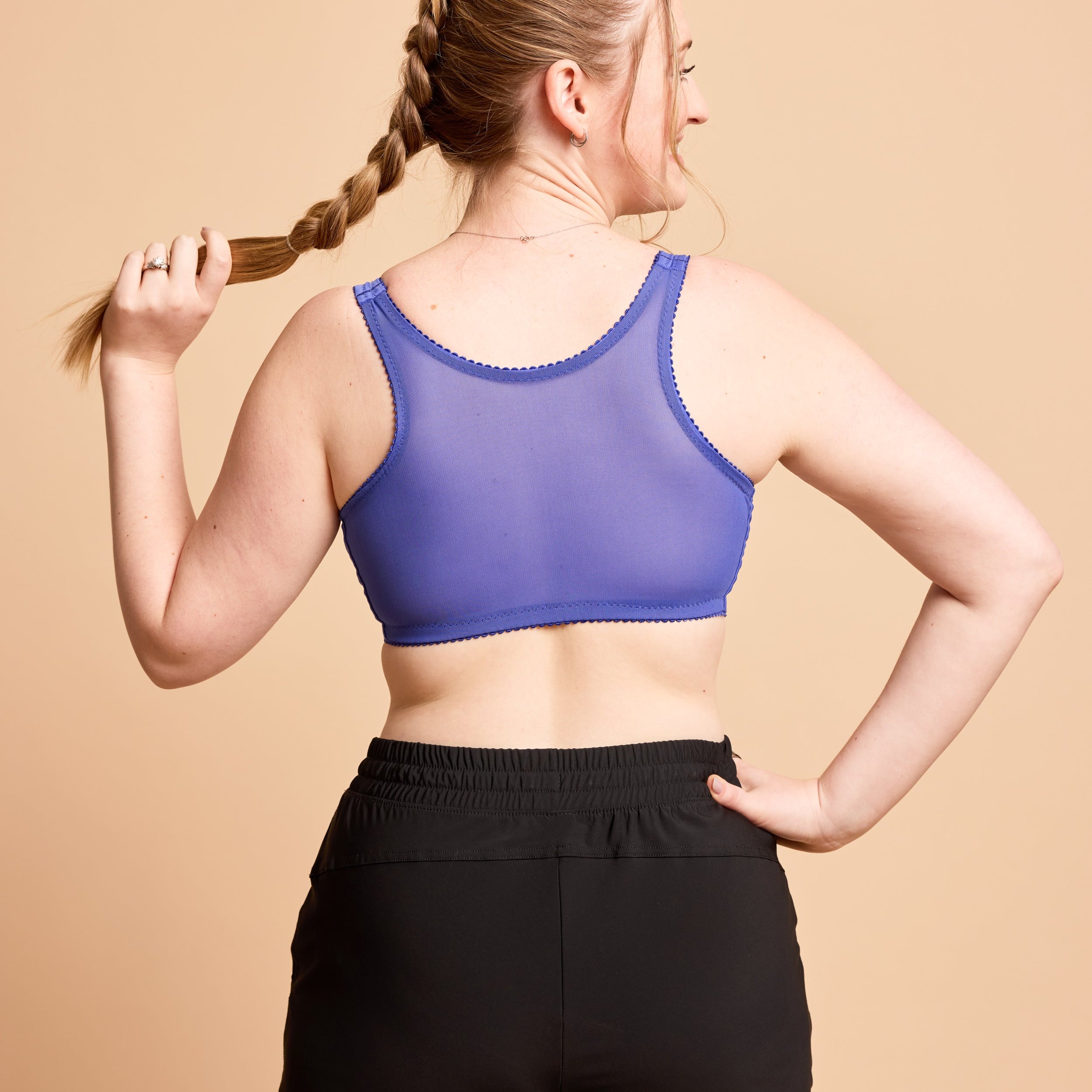 Woman wearing a purple sports bra and black leggings against a beige background. This is the Cashmerette Somerville Sports Bra sewing pattern for big boobs.