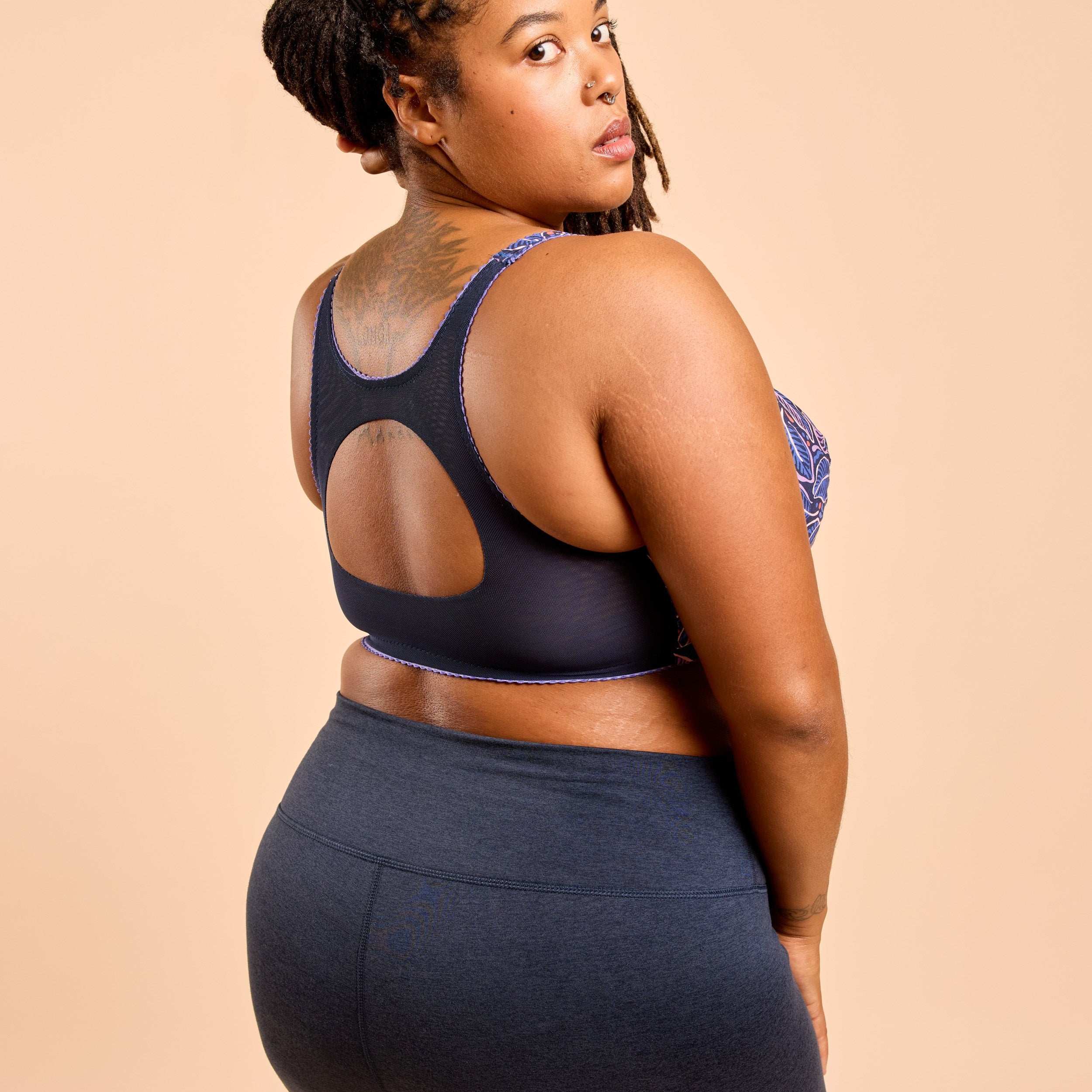 Woman wearing a black sports bra and leggings on a beige background. This is the Cashmerette Somerville Sports Bra sewing pattern for big boobs.