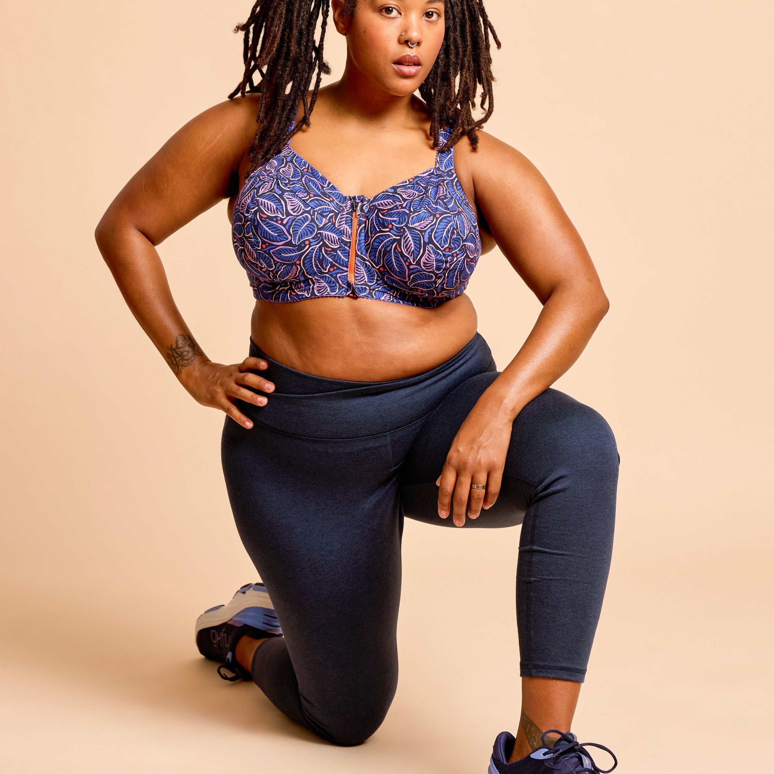Woman wearing a blue patterned sports bra and navy leggings on a beige background. This is the Cashmerette Somerville Sports Bra sewing pattern for big boobs.