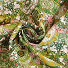 A close-up of a patterned fabric rolled into a spiral, showing a detailed botanical and animal print in shades of green, pink, white, and yellow.