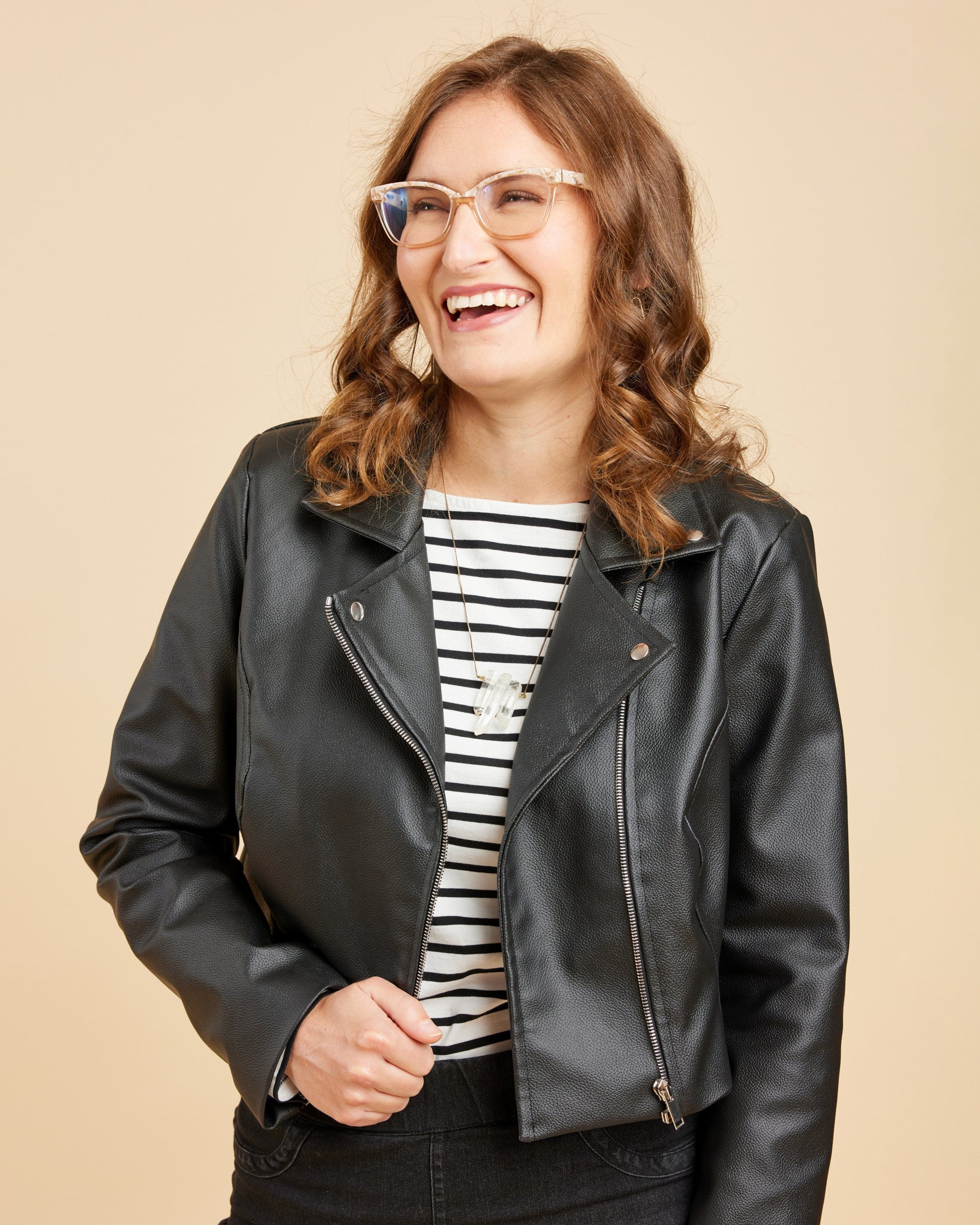 Woman wearing a black leather jacket over a striped shirt on a beige background. This biker jacket is the Canton Moto Jacket sewing pattern from Cashmerette.