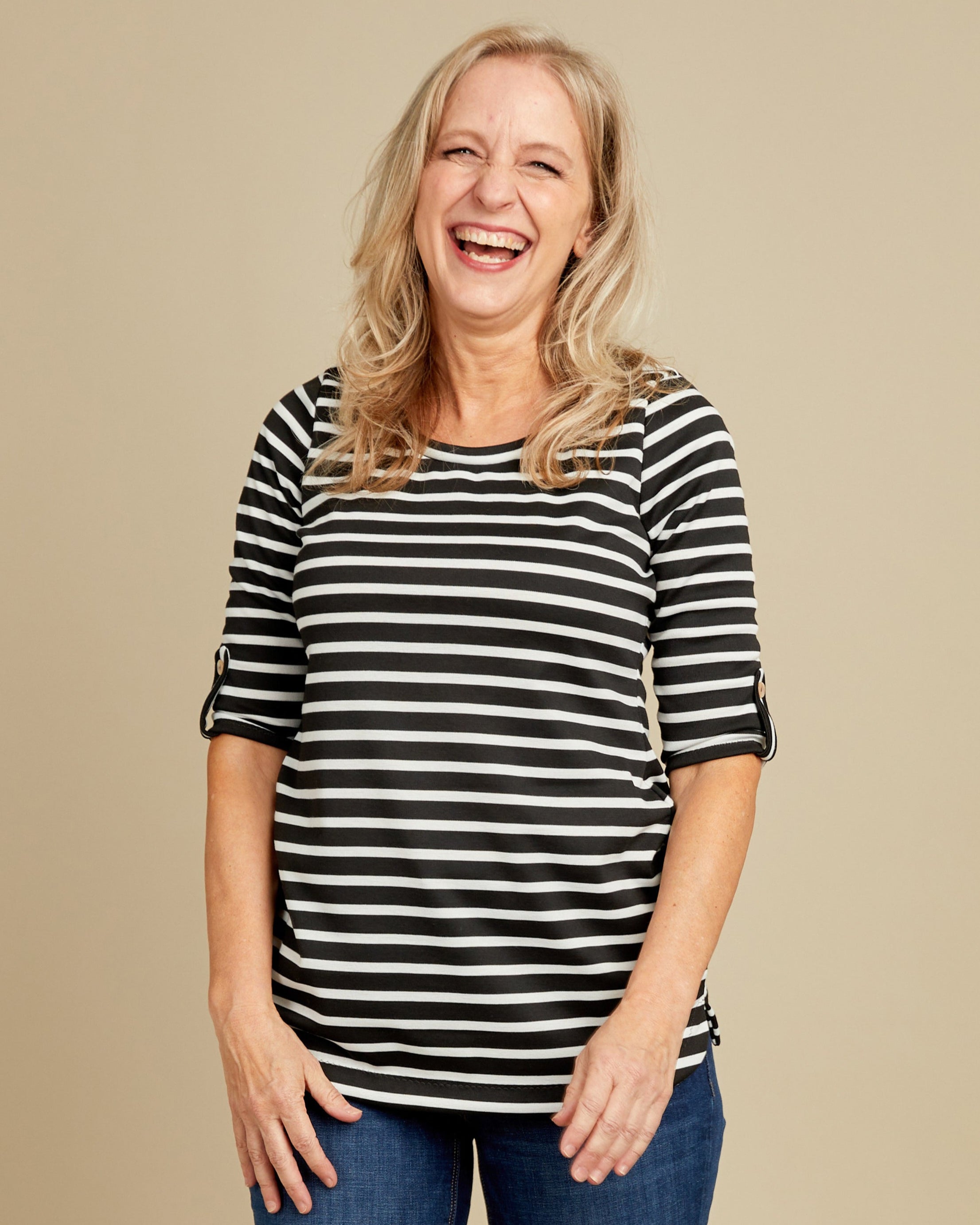 Woman wearing a black and white striped shirt and blue jeans on a beige background. This t-shirt is the Concord T-Shirt sewing pattern from Cashmerette.