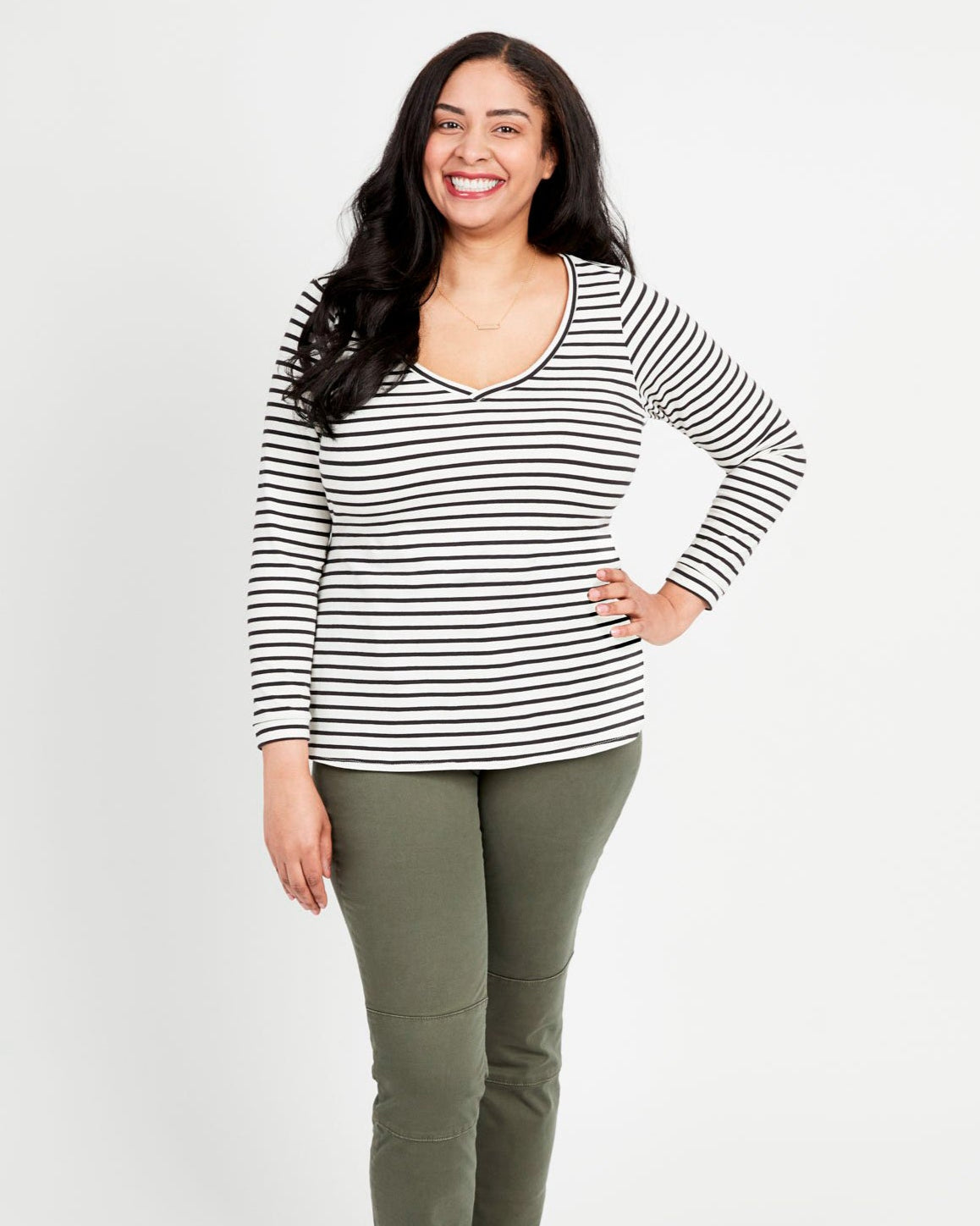 A woman standing, wearing a striped long-sleeved t-shirt and green pants. This t-shirt is the Concord T-Shirt sewing pattern from Cashmerette.