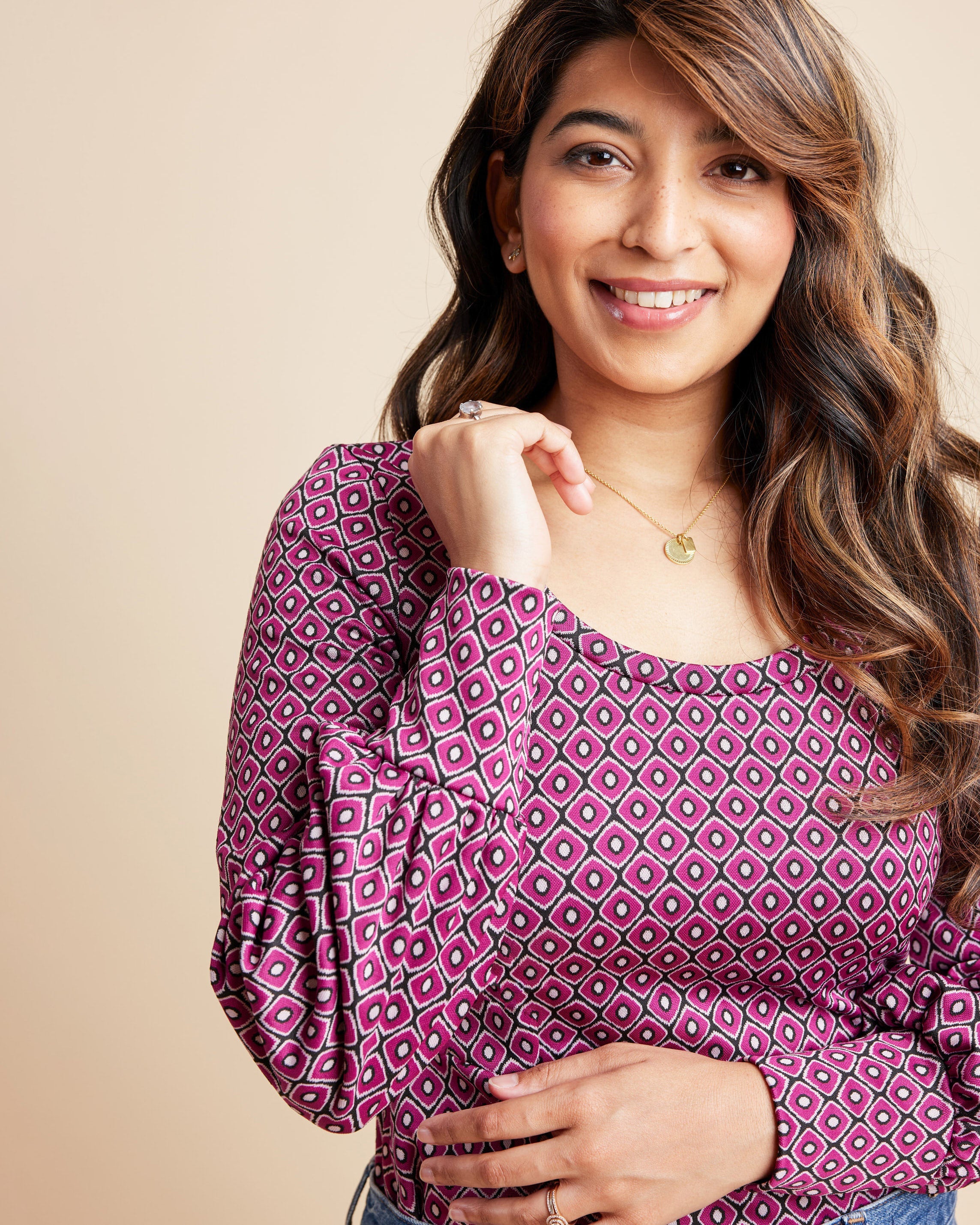 Woman wearing a patterned pink blouse against a beige background. This is the Grafton Dress, Top & Skirt sewing pattern from Cashmrette.