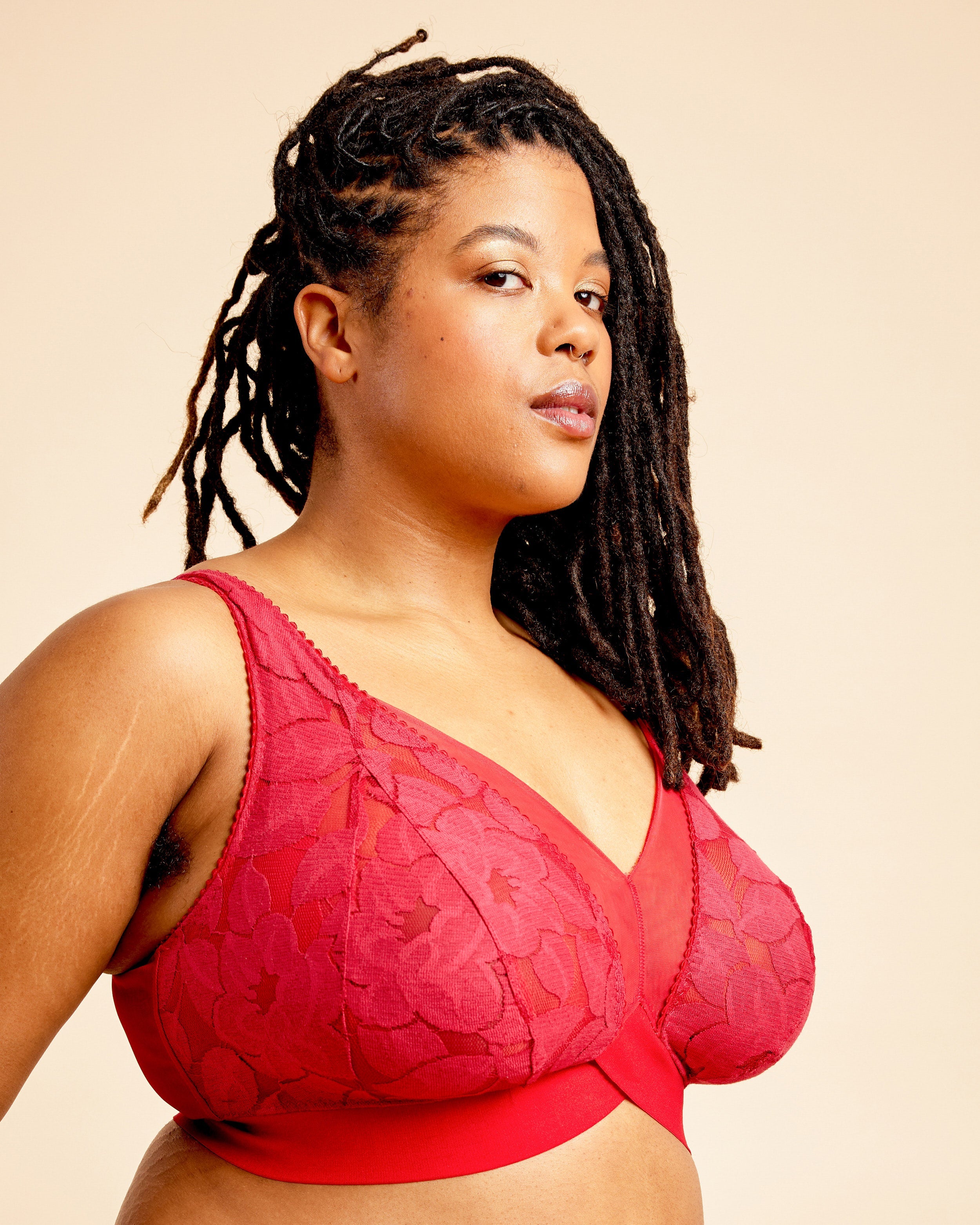Woman wearing a red lace bralette against a beige background. This bralette is the Loftus Bralette sewing pattern from Cashmerette.