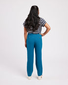 Person wearing blue pants and a striped shirt on a white background. These pants are the Meriam Trousers sewing pattern from Cashmerette.