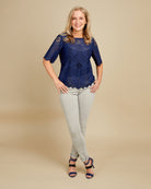 Woman wearing a blue lace top and light gray pants on a beige background. This top is the Montrose Top sewing pattern from Cashmerette.