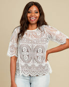 Woman wearing a white lace top against a beige background. This top is the Montrose Top sewing pattern from Cashmerette.
