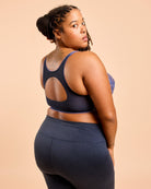 Woman wearing a black sports bra and leggings on a beige background. This is the Cashmerette Somerville Sports Bra sewing pattern for big boobs.